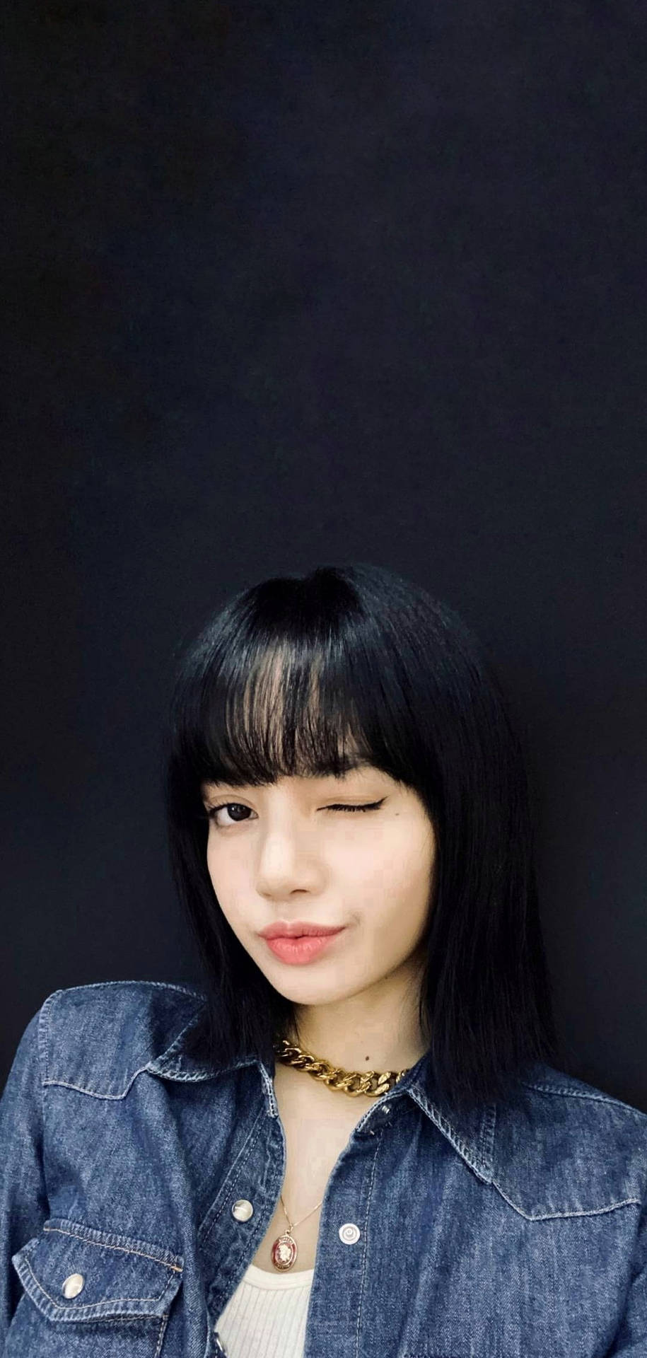 年輕女性身穿牛仔外套戴金鏈在深色背景前眨眼 — BLACKPINK Lisa GIF 壁紙