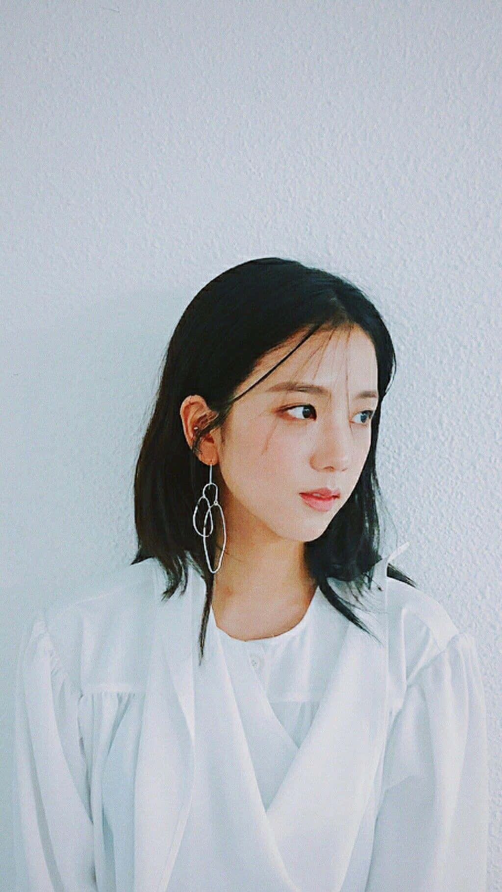 BLACKPINK 桌布 壁紙 — 一位黑髮戴銀耳環的年輕女子，穿著白色襯衫，對著白牆若有所思地凝視。