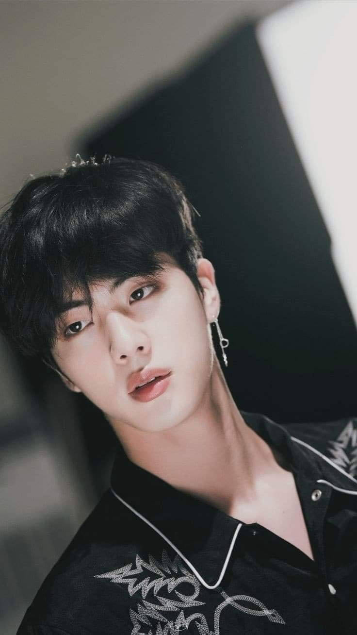 kim seok jin 桌布 壁紙 — 一位黑髮戴銀耳環的年輕男子，穿著黑色刺繡襯衫，在簡約的攝影棚背景下溫柔地凝視鏡頭。