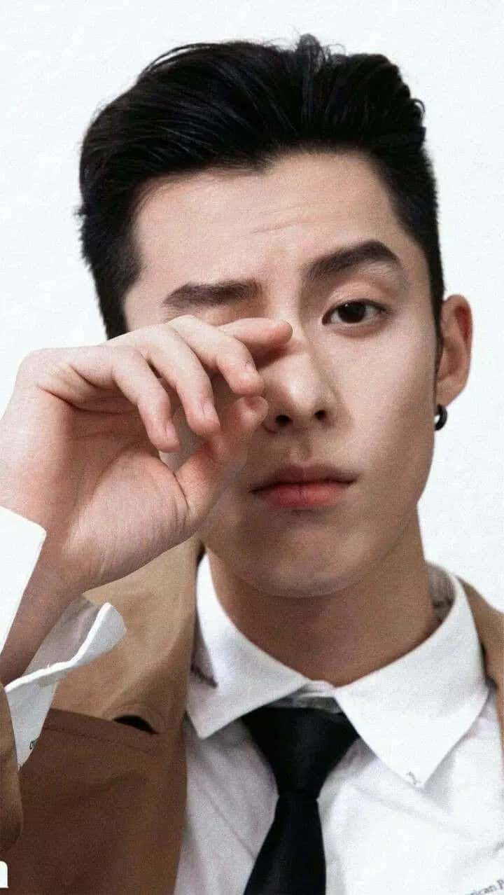 Dylan Wang 桌布 壁紙 — 一位黑髮戴黑色耳環的年輕男子，在純白背景前專注地舉手靠近眼睛。