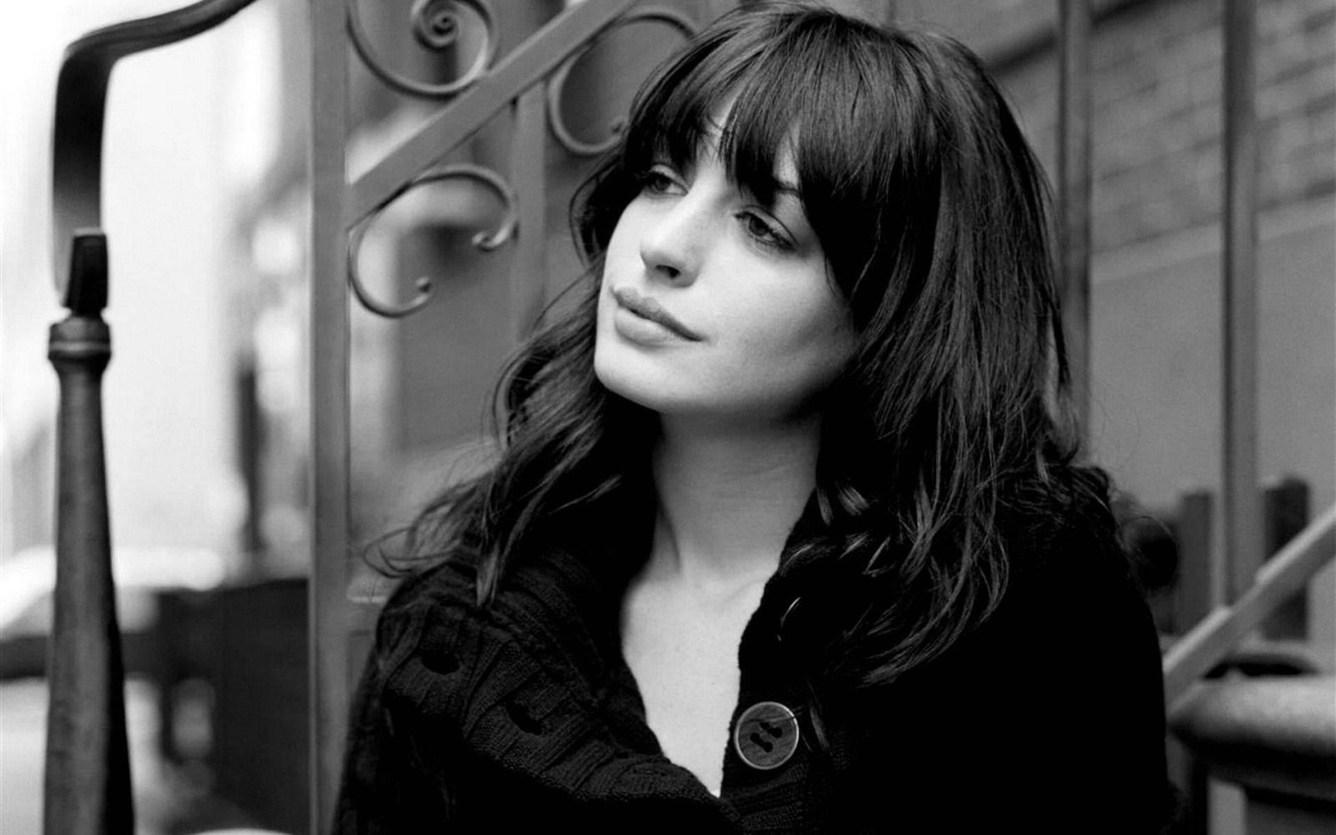 Anne Hathaway 桌布 壁紙 — 一位黑髮有瀏海的女性在華麗金屬欄杆旁向上凝視的黑白肖像。