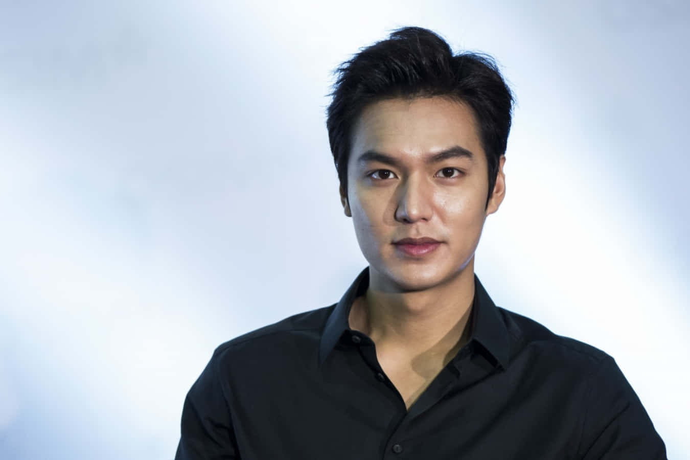 Lee Min Ho 桌布 壁紙 — 一位黑髮濃密、眼神銳利的俊男，在柔和漸變背景前穿著黑色襯衫。