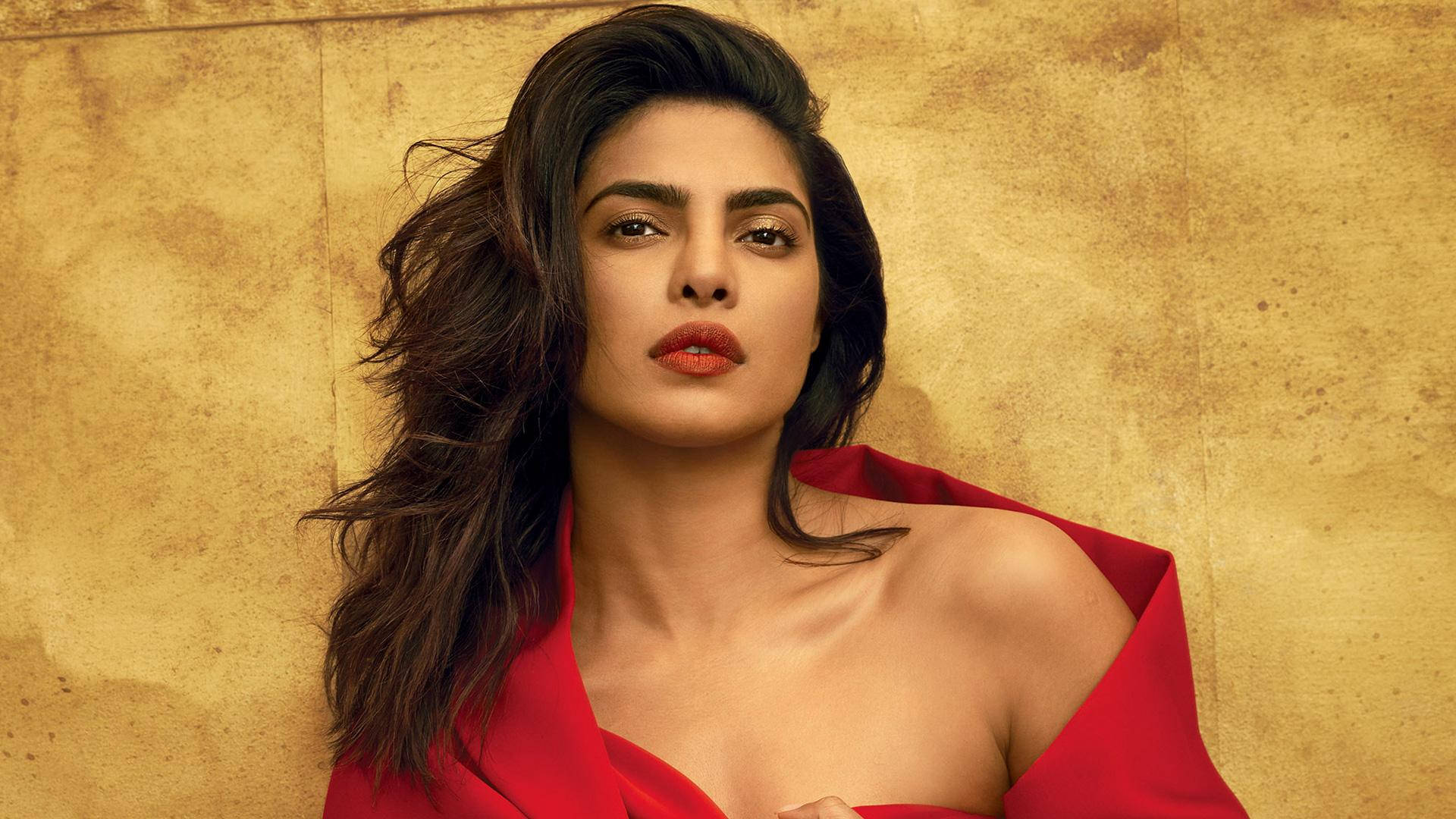 Priyanka 桌布 壁紙 — 一位黑髮紅唇的女性，在帶有紋理的金色背景前穿著大膽的紅色服裝。