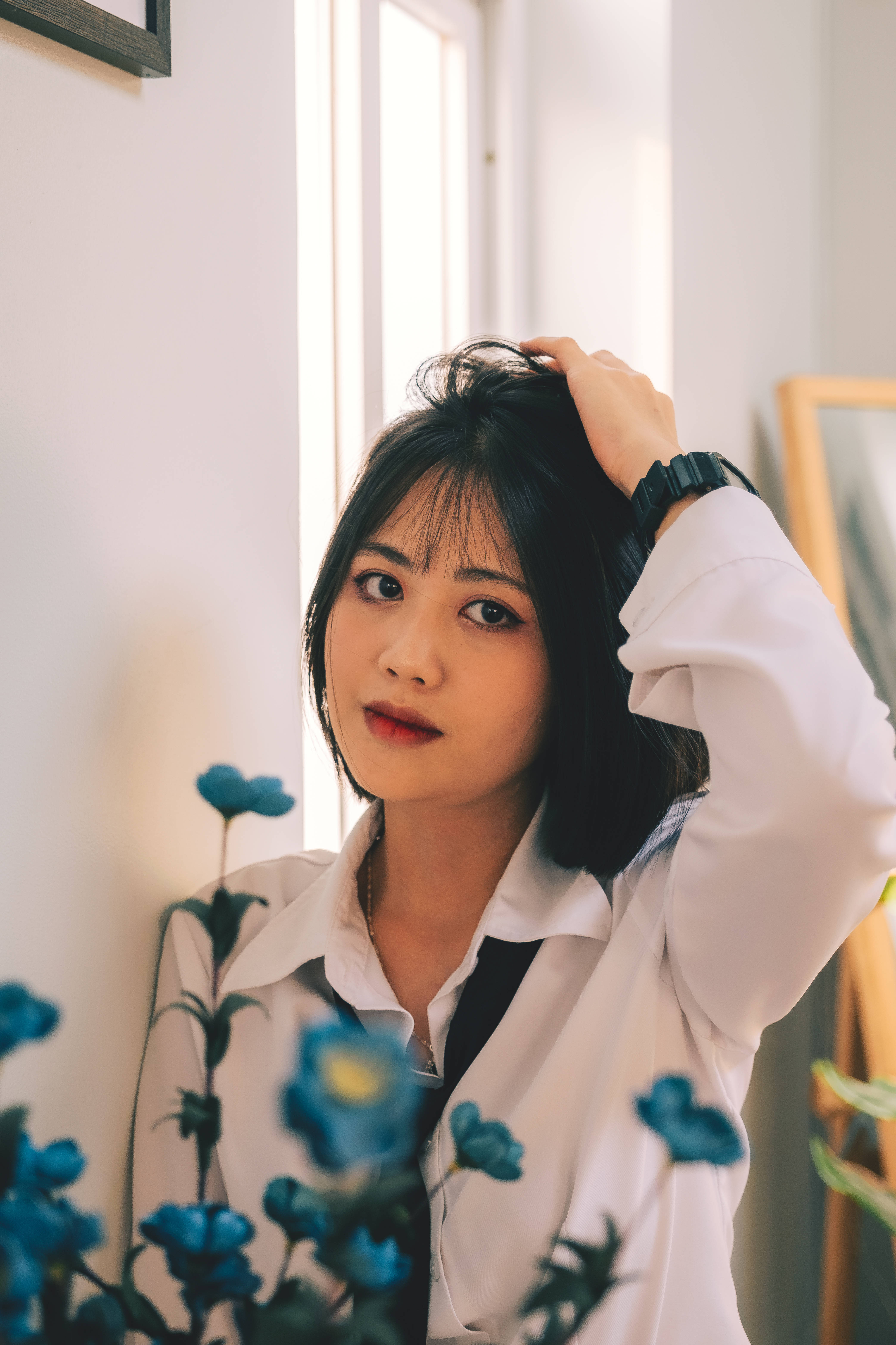 Beautiful Cute 桌布 壁紙 — 一位黑髮紅唇的年輕女性，在前景有藍色花朵的窗邊輕柔地撫摸頭髮，眼神柔和。