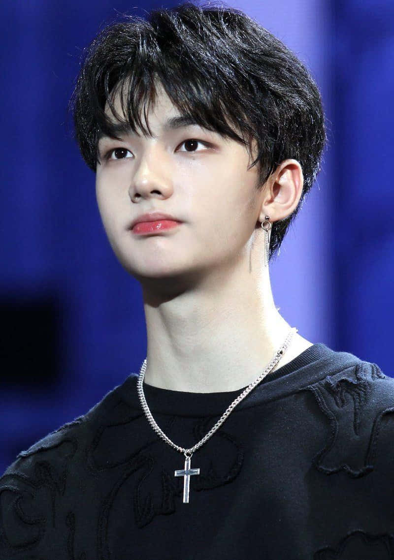 hyunjin 桌布 壁紙 — 一位黑髮紅唇的年輕男子，在深藍色模糊背景前若有所思地凝視。