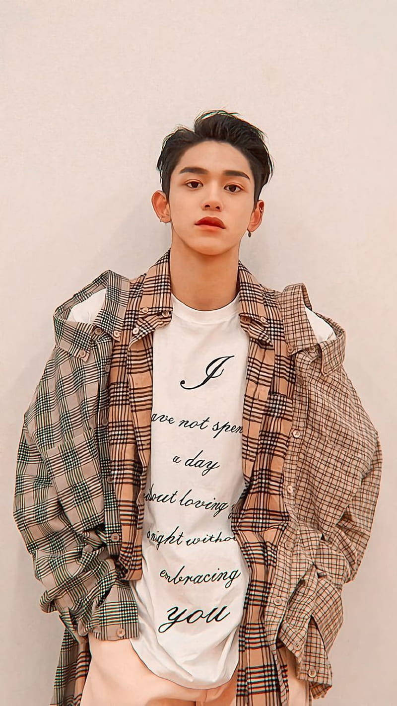 Nct 桌布 壁紙 — 一位黑髮紅唇的年輕男子，穿著一件開襟格紋襯衫，內搭白色T恤，上面有草書文字，背景是純色米色牆壁。