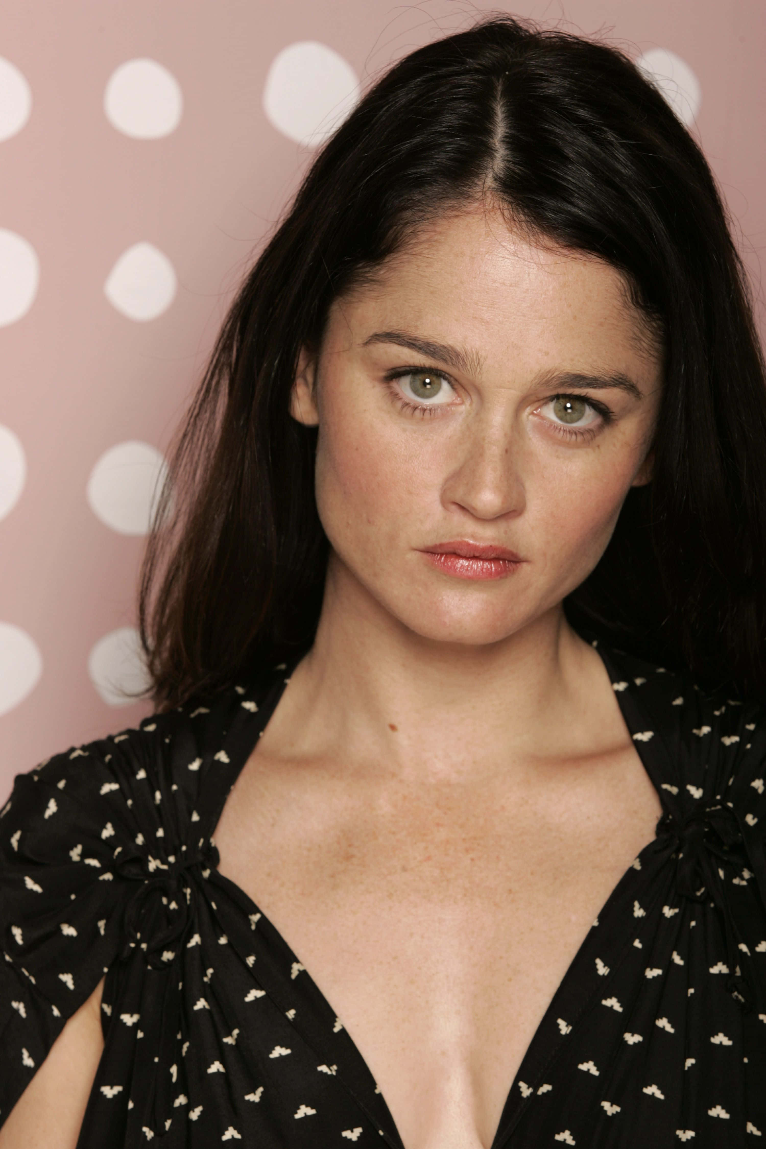 Robin Tunney 桌布 壁紙 — 一位黑髮綠眼的女性在粉紅色圓點背景前直視鏡頭。