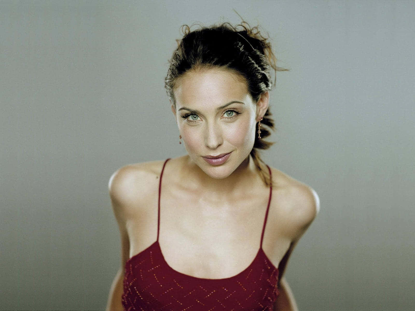 Claire Forlani 桌布 壁紙 — 一位黑髮綠眼的女性穿著紅色圖案上衣，背景是純灰色。