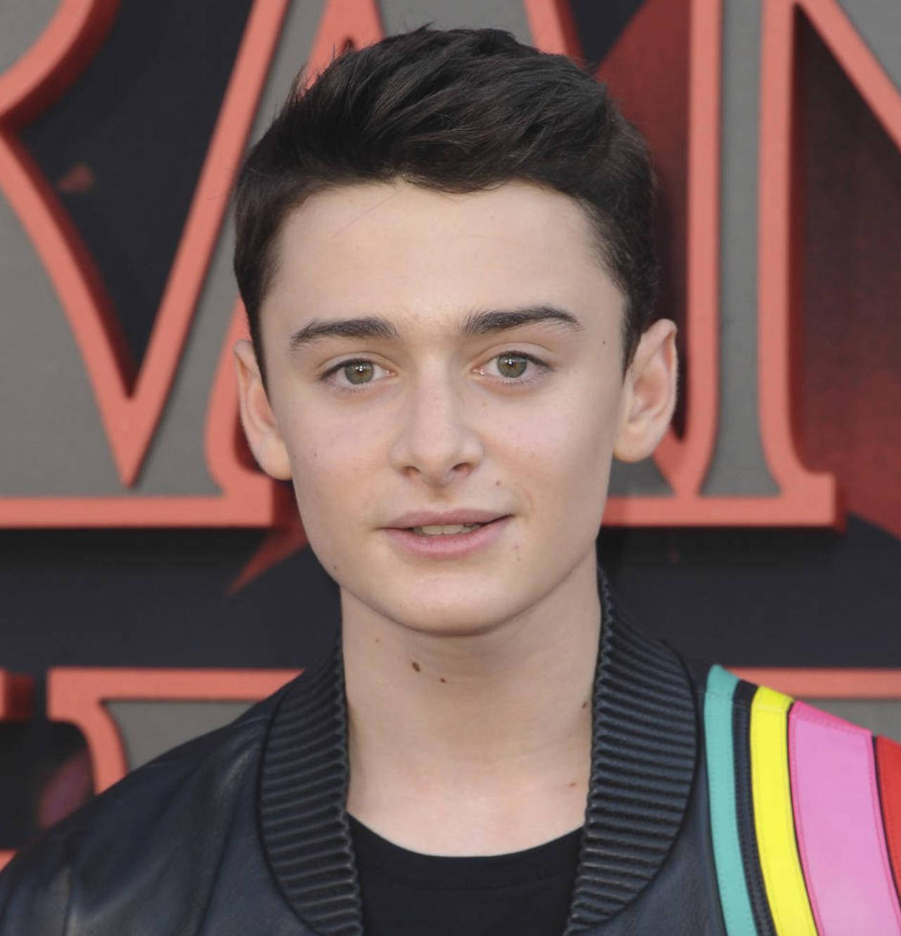 Celebrity 桌布 壁紙 — 一位黑髮綠眼的年輕男子穿著黑色皮夾克，肩上有彩色條紋點綴，背景是紅色和灰色的活動背景。