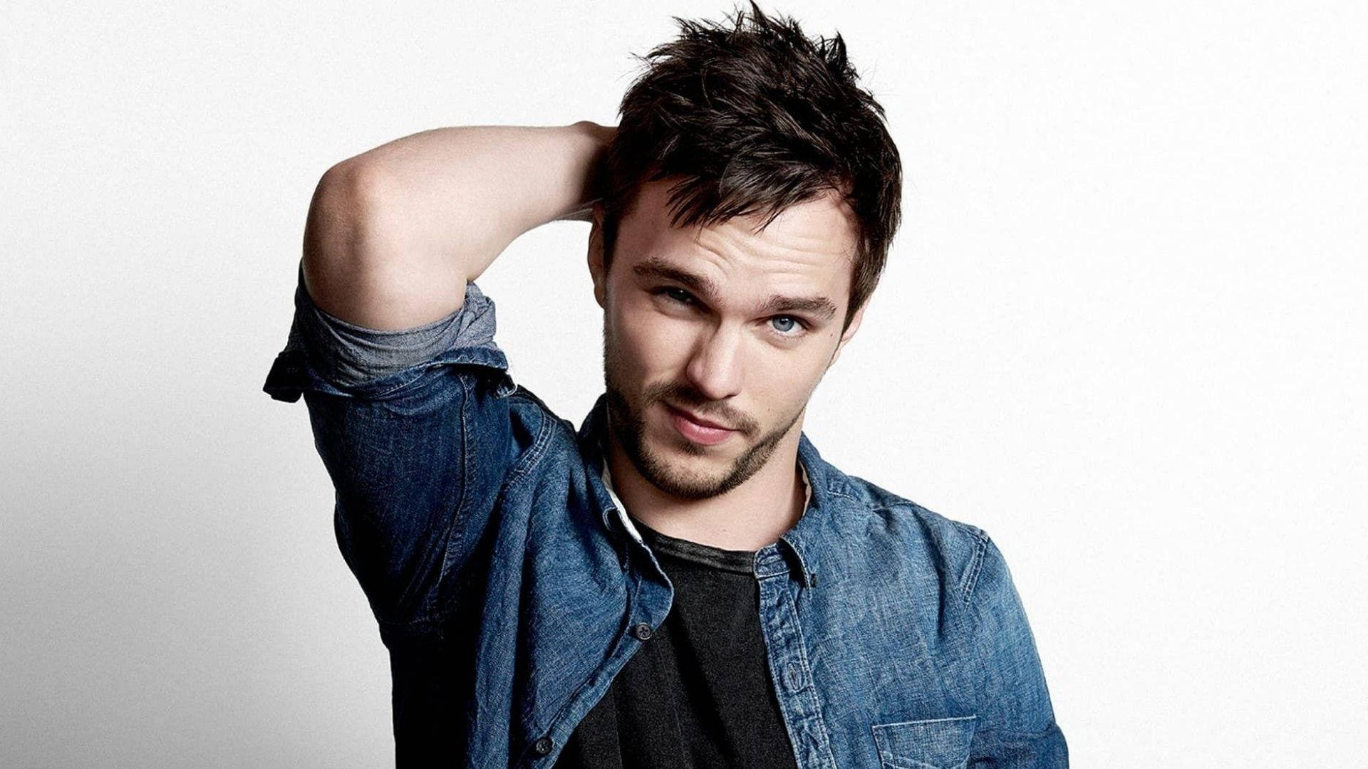 Nicholas Hoult 桌布 壁紙 — 一位黑髮藍眼的年輕男子穿著牛仔襯衫，在純白背景前擺姿勢。