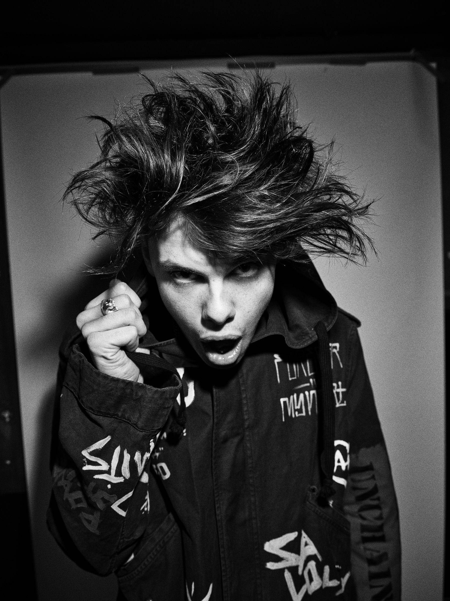 Yungblud 桌布 壁紙 — 一位龐克搖滾音樂家，頭髮狂野，表情強烈，身穿塗鴉外套，在黑白工作室肖像中。