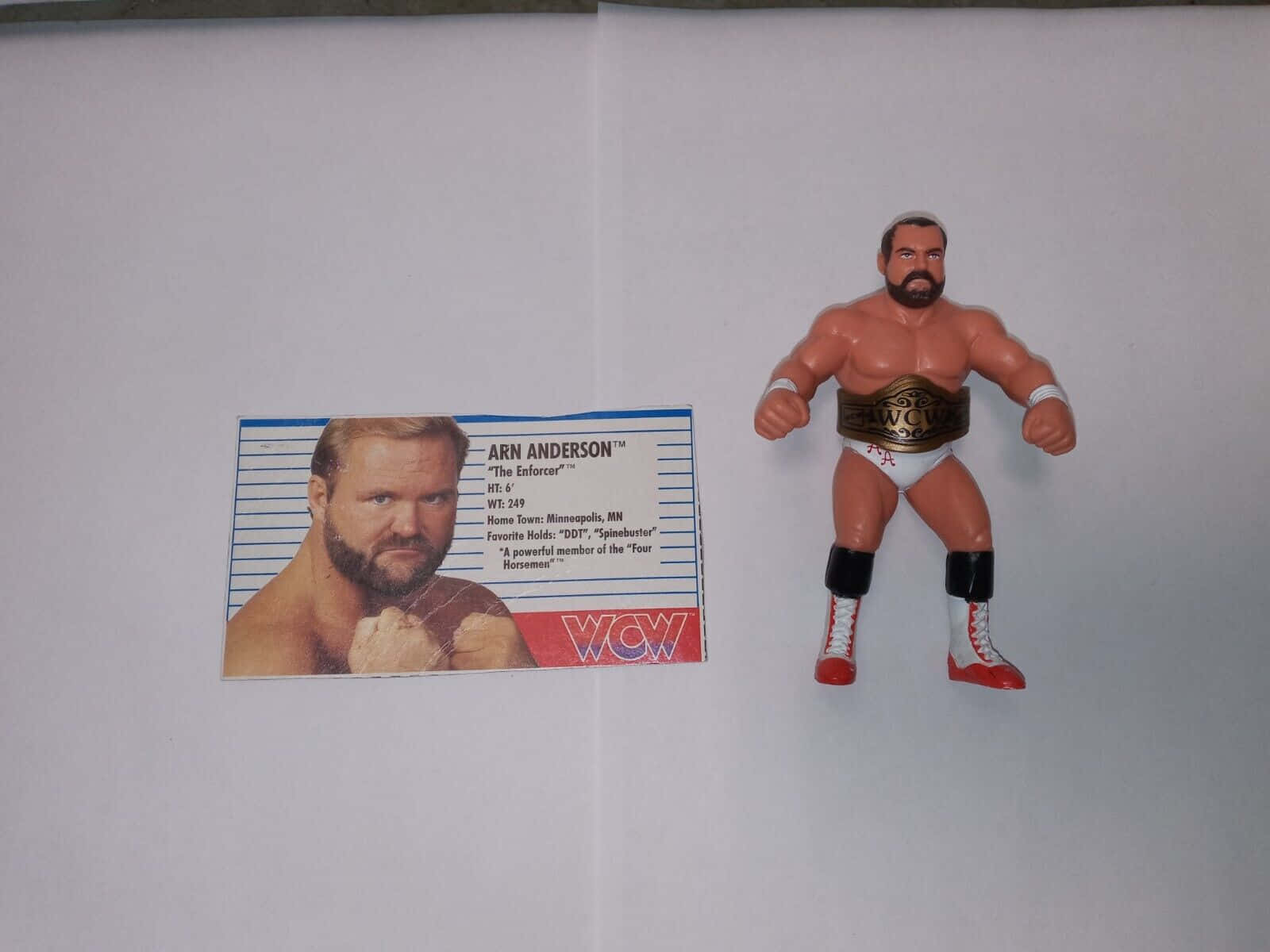Champion 桌布 壁紙 — 一個 Arn Anderson 的 WCW 摔角動作人偶站在他的官方交換卡旁邊，置於純白色表面上。