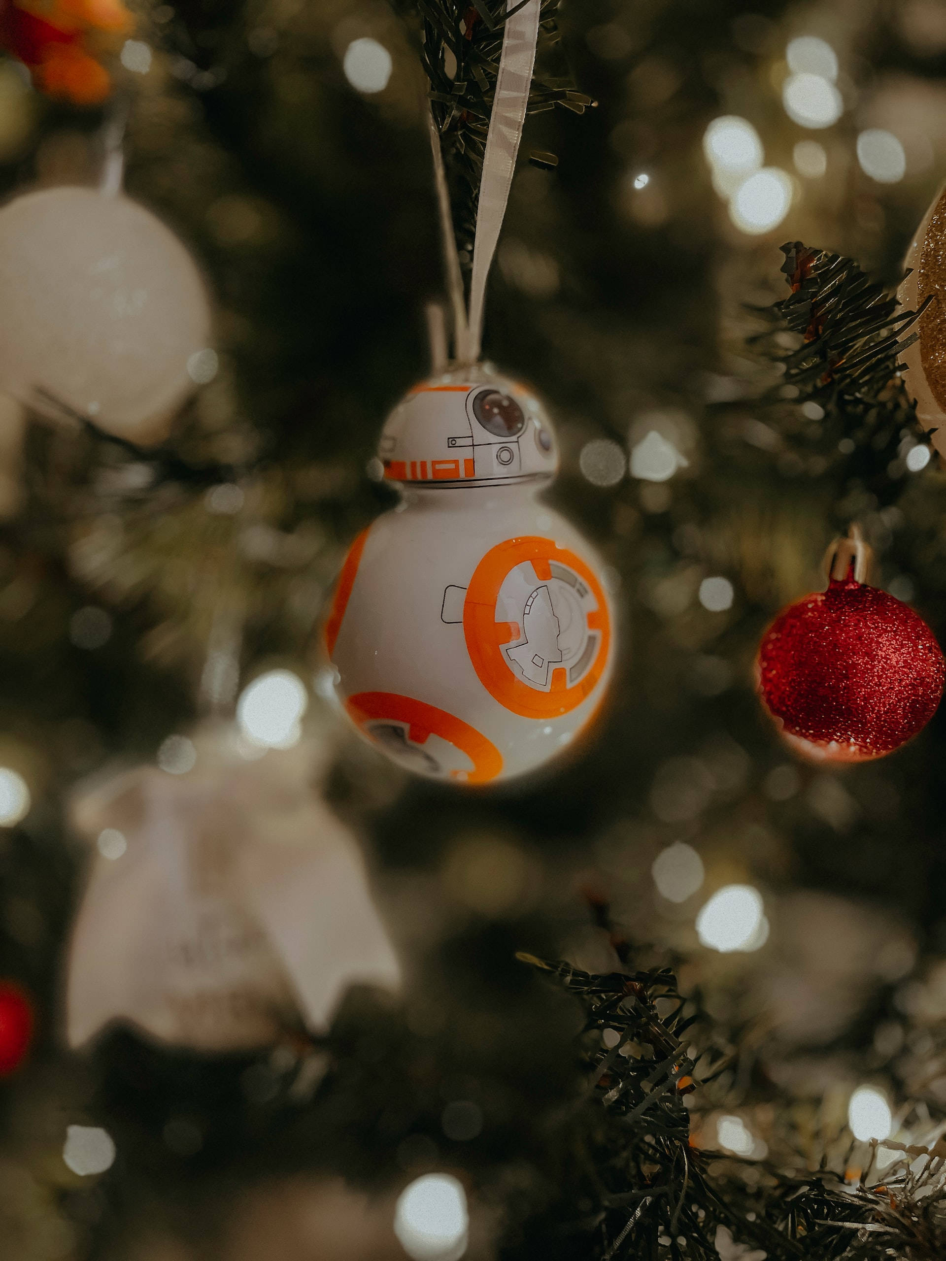 星際大戰 iPhone 桌布 壁紙 — 一個 BB-8 星際大戰裝飾品掛在柔和燈光的聖誕樹上，配有散景燈光和其他節日飾物。