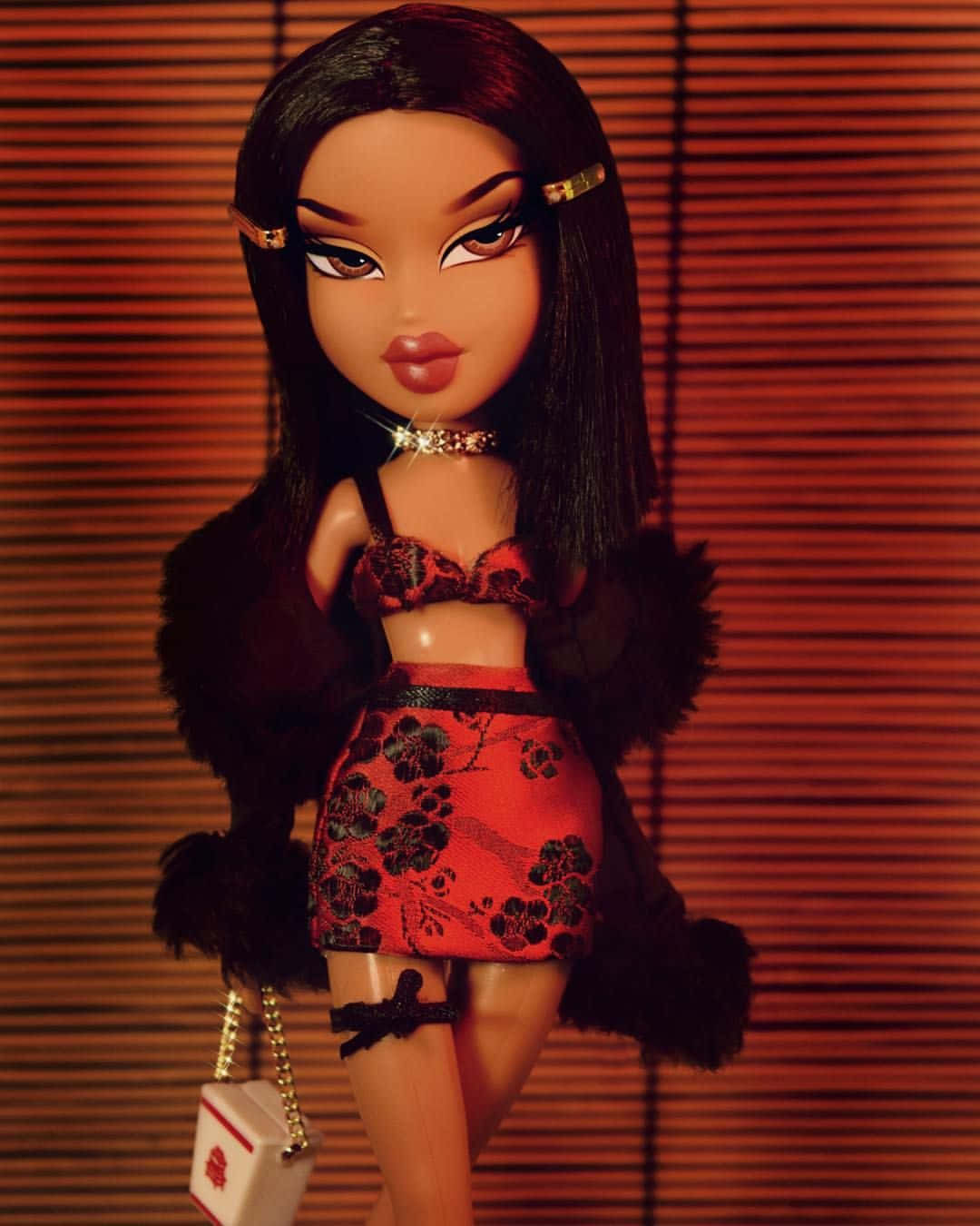 Bratz 桌布 壁紙 — 一個 Bratz 娃娃穿著紅色花卉服裝和黑色毛皮披肩，在溫暖的木百葉窗前拿著時尚手提包擺姿勢。