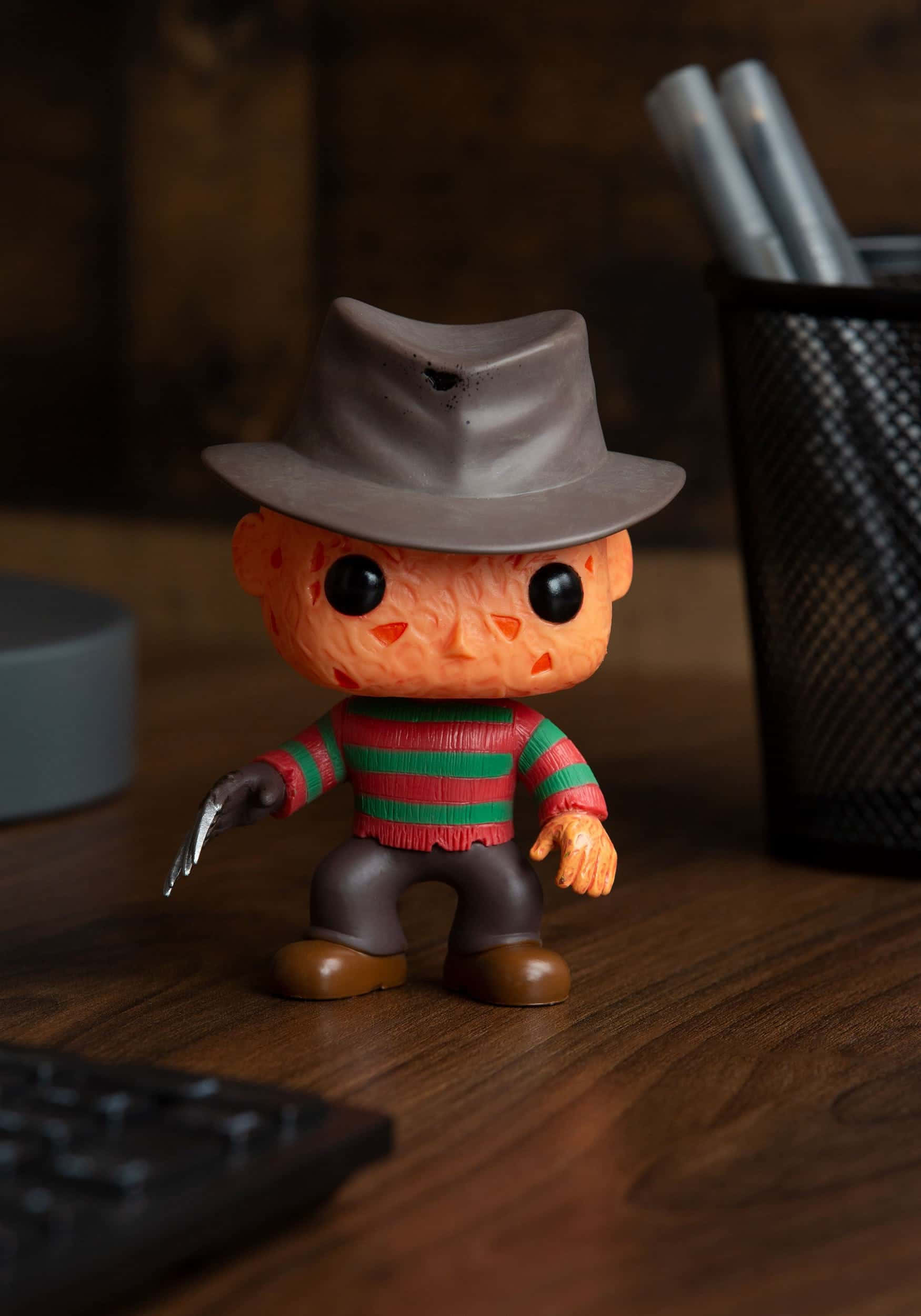 佛莱迪·克鲁格 桌布 壁紙 — 一個 Freddy Krueger Funko Pop! 人偶站在木桌上，旁邊有鍵盤和筆筒。