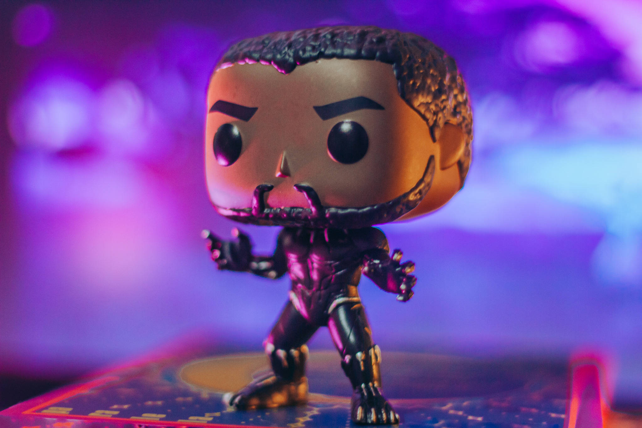 pop 桌布 壁紙 — 一個 Funko Pop 黑豹人偶在充滿活力的紫色和藍色散景背景前擺好姿勢。