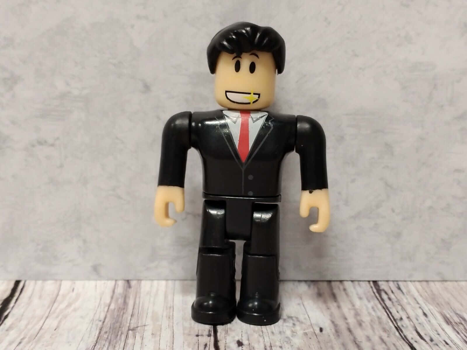 桌布 壁紙 — 一個 Roblox 風格的商人公仔，身穿黑色西裝和紅色領帶，站在一個風化的木質表面上，背景是灰色大理石紋牆。