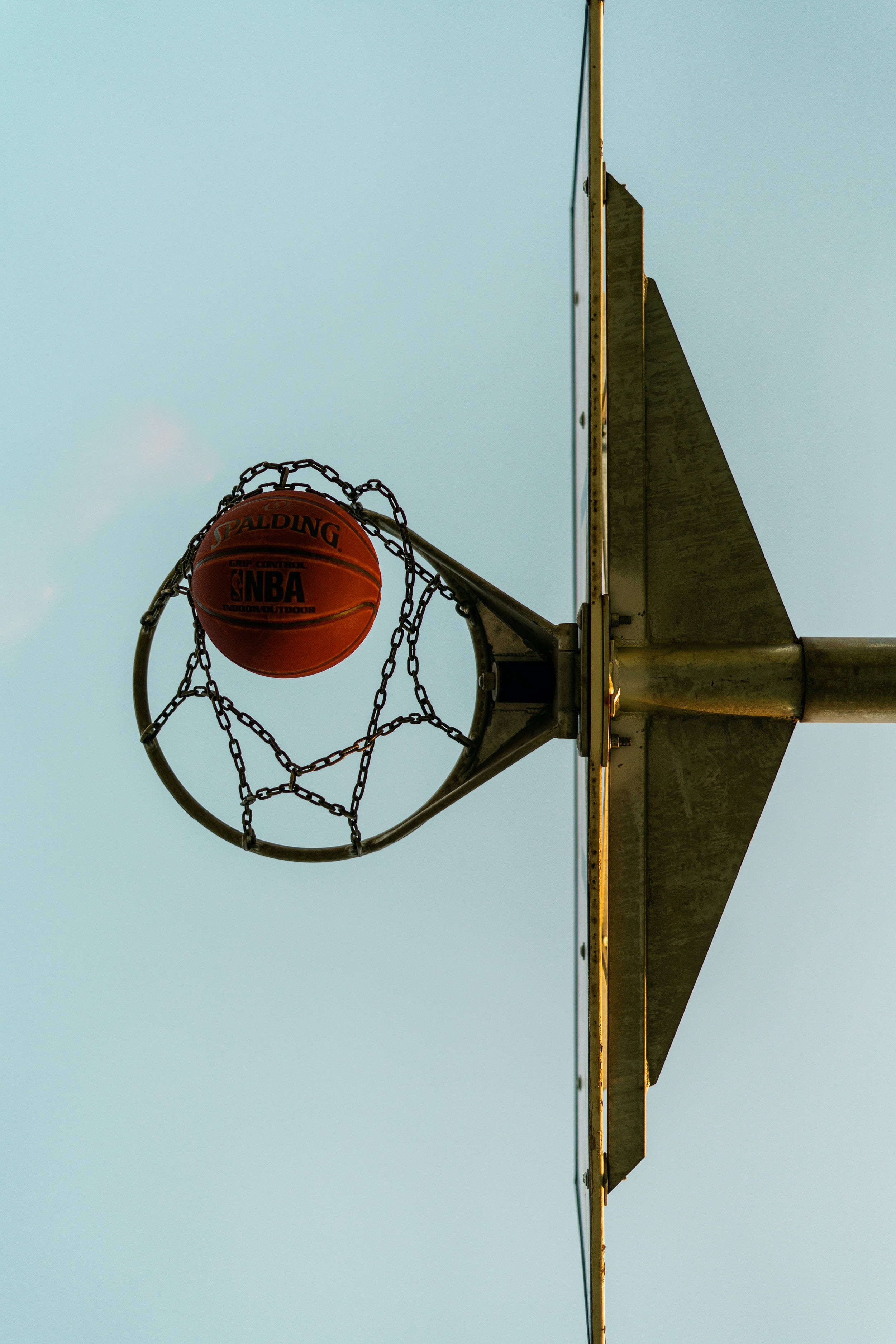 籃球 桌布 壁紙 — 一個 Spalding NBA 籃球完美地掛在鏈網籃框上，背景是清澈的淡藍色天空。