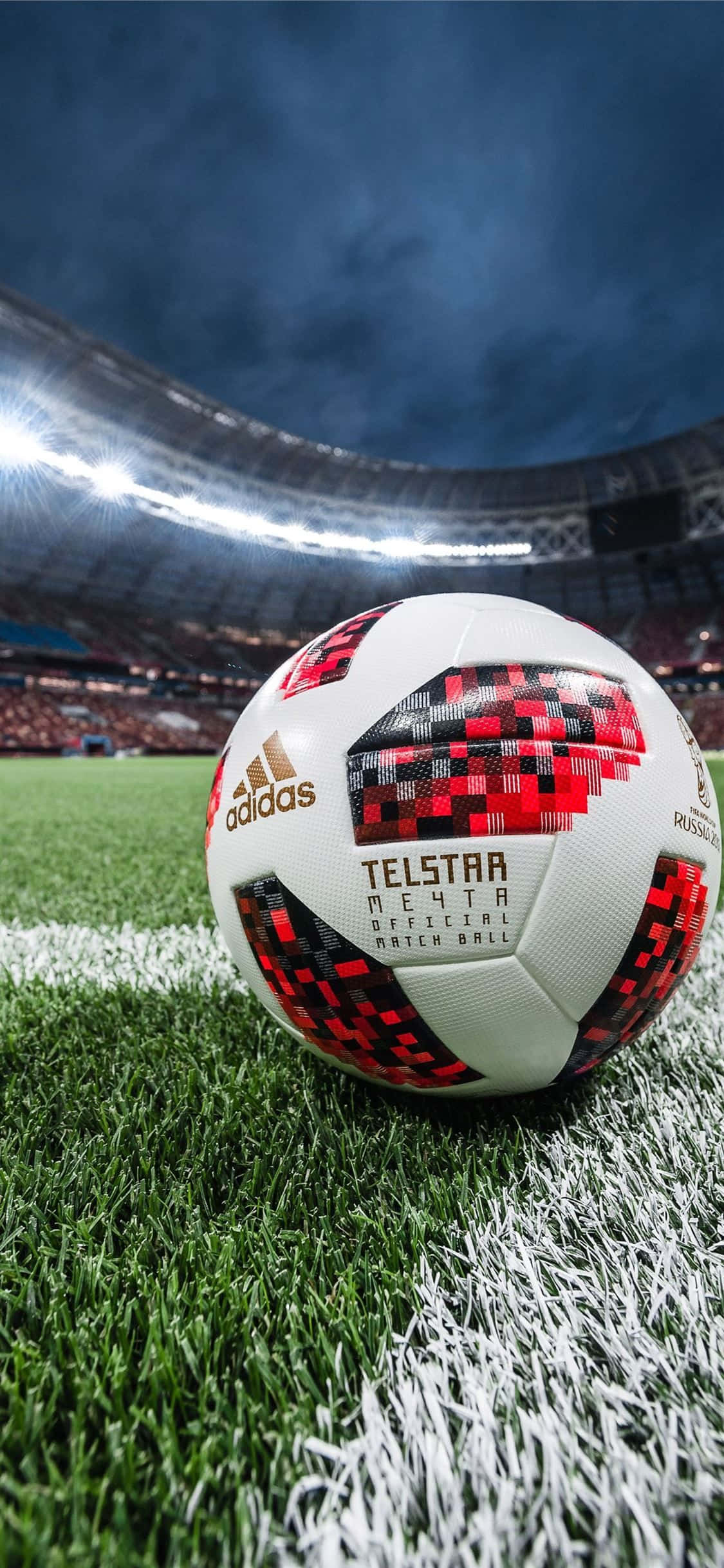 足球 桌布 壁紙 — 一個 Telstar 18 足球放在充滿活力的綠色草地上，背景是球場燈光下模糊的人群。