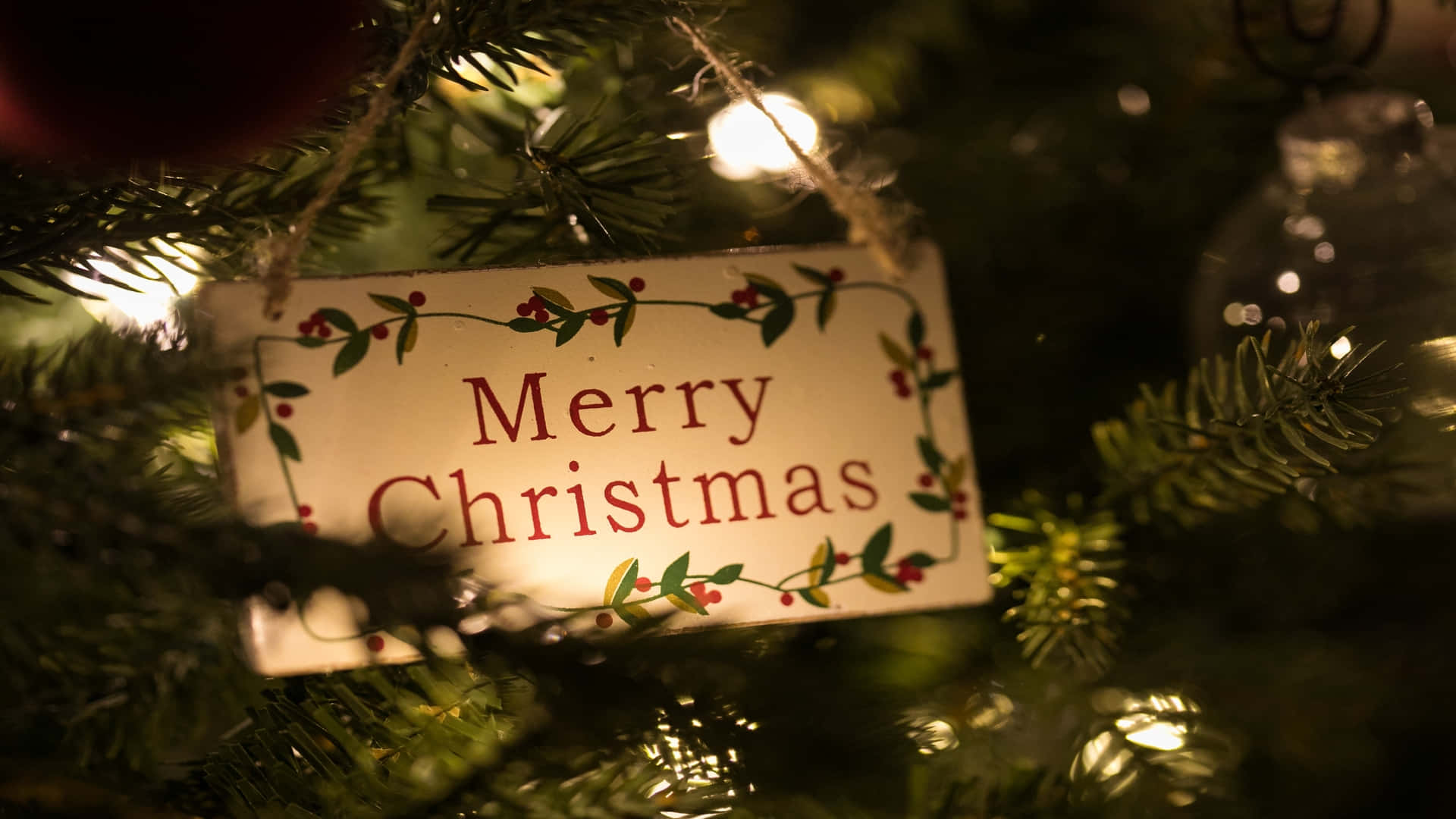 節日 桌布 壁紙 — 一個「聖誕快樂」標牌的特寫，藏在裝飾樹的松針和閃爍的仙女燈之間。