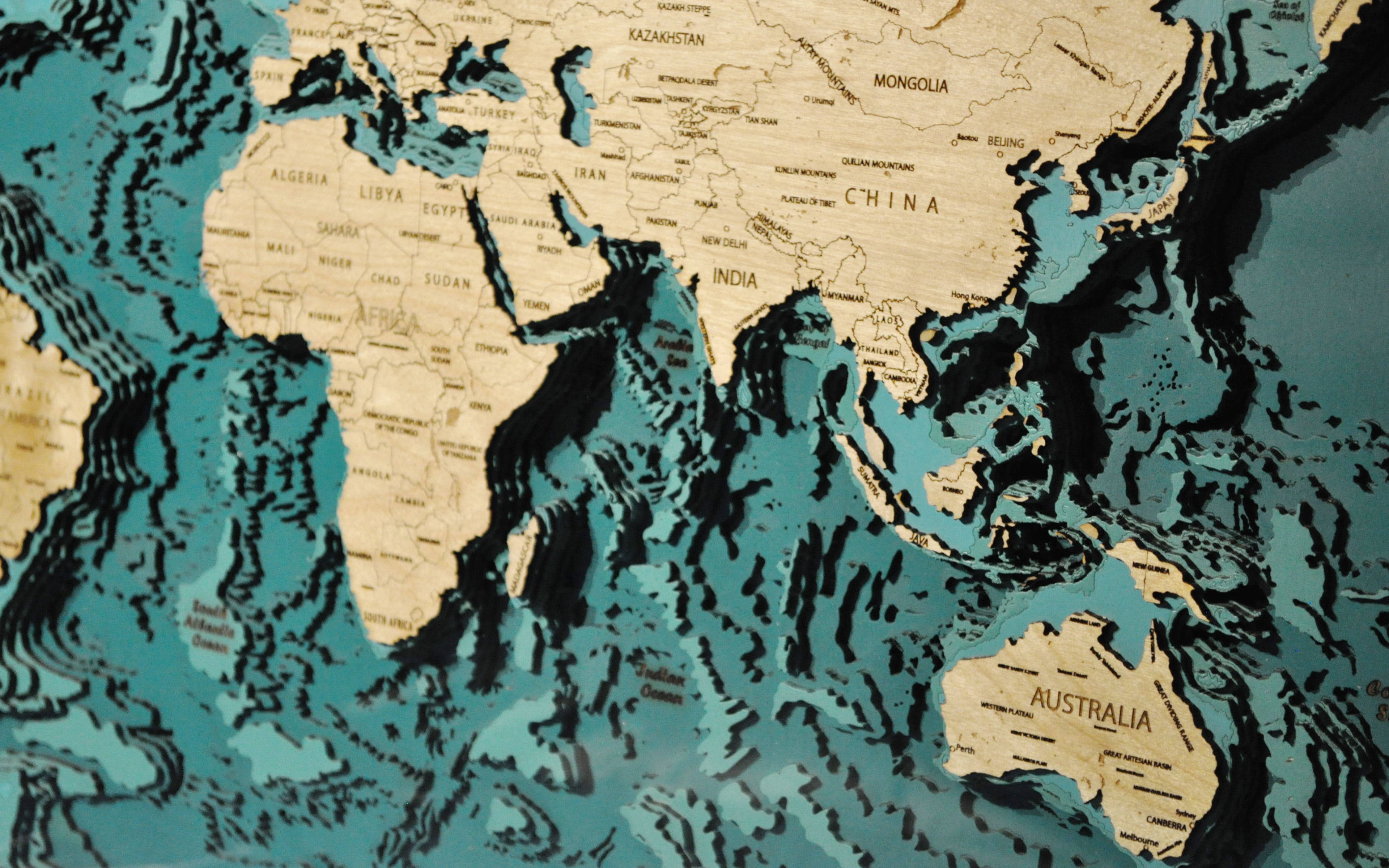Topographic 桌布 壁紙 — 一個3D木製世界地圖，大陸為淺色木材，海洋為帶紋理的青綠色。