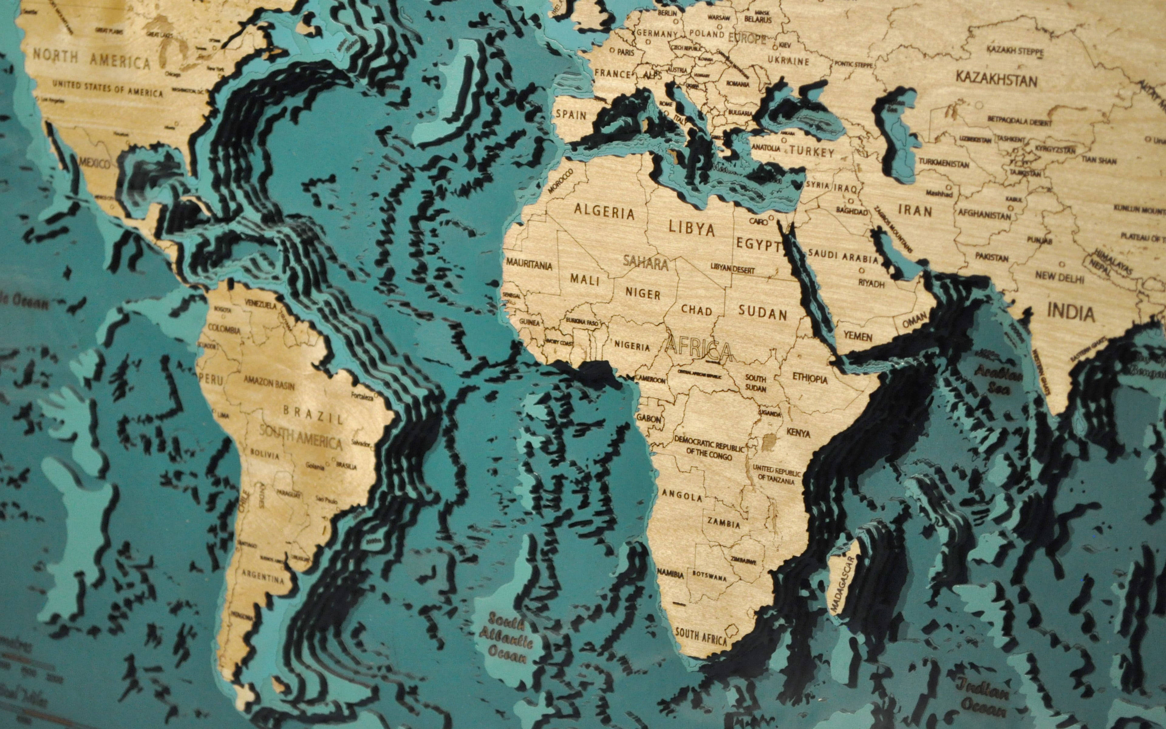 世界地圖 桌布 壁紙 — 一個3D木製世界地圖，帶有雕刻的大陸和藍綠色海洋，顯示非洲及周邊地區。