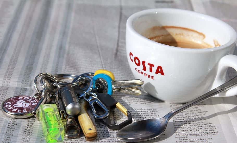Utensils 桌布 壁紙 — 一個Costa Coffee杯和鑰匙放在報紙上，附近有一隻湯匙。