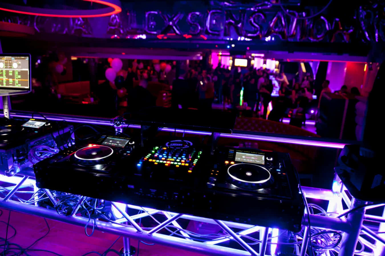 Nightclub 桌布 壁紙 — 一個DJ台沐浴在充滿活力的紫色和藍色霓虹燈光中，背後可見擁擠的夜總會場景。