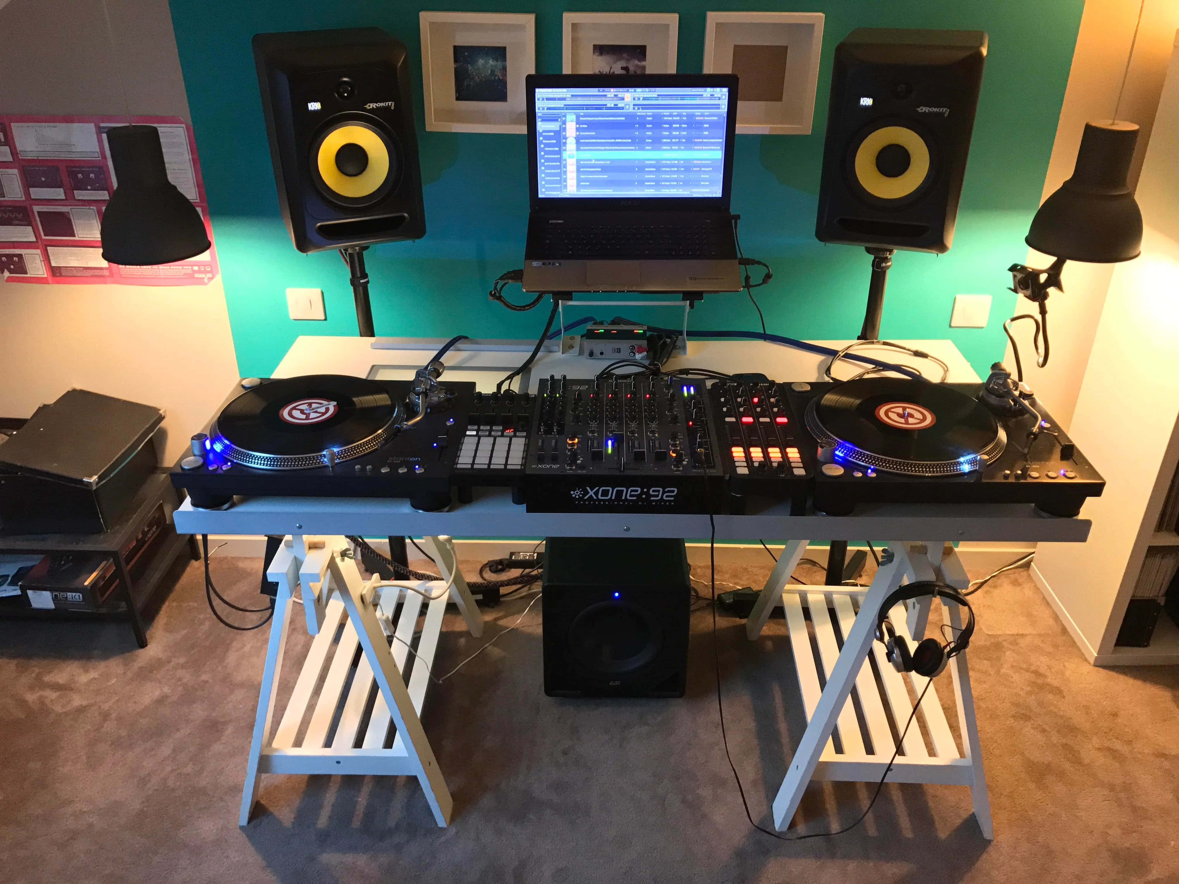 音樂 桌布 壁紙 — 一個DJ設置，包含兩個唱盤、一個混音器、筆記型電腦和揚聲器，排列在白色桌子上，背景是青綠色牆壁。