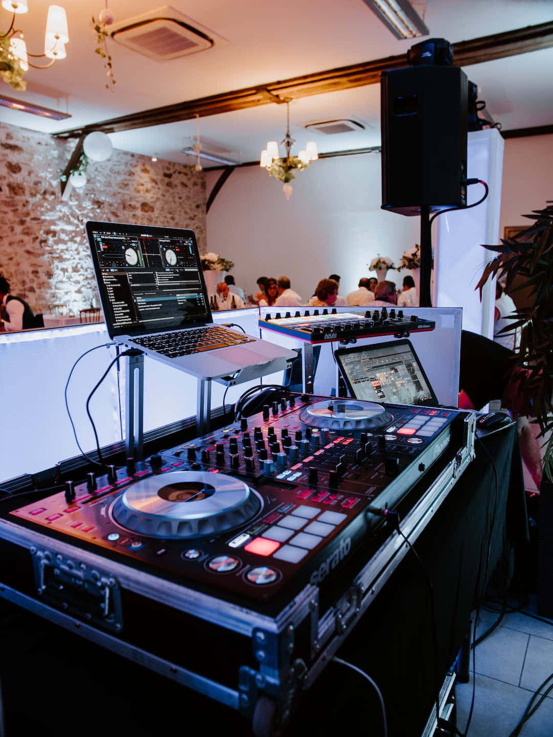 DJ 桌布 壁紙 — 一個DJ設置，配有發光的紅色控制器和筆記型電腦，在一個熱鬧的室內派對中，背景有賓客。