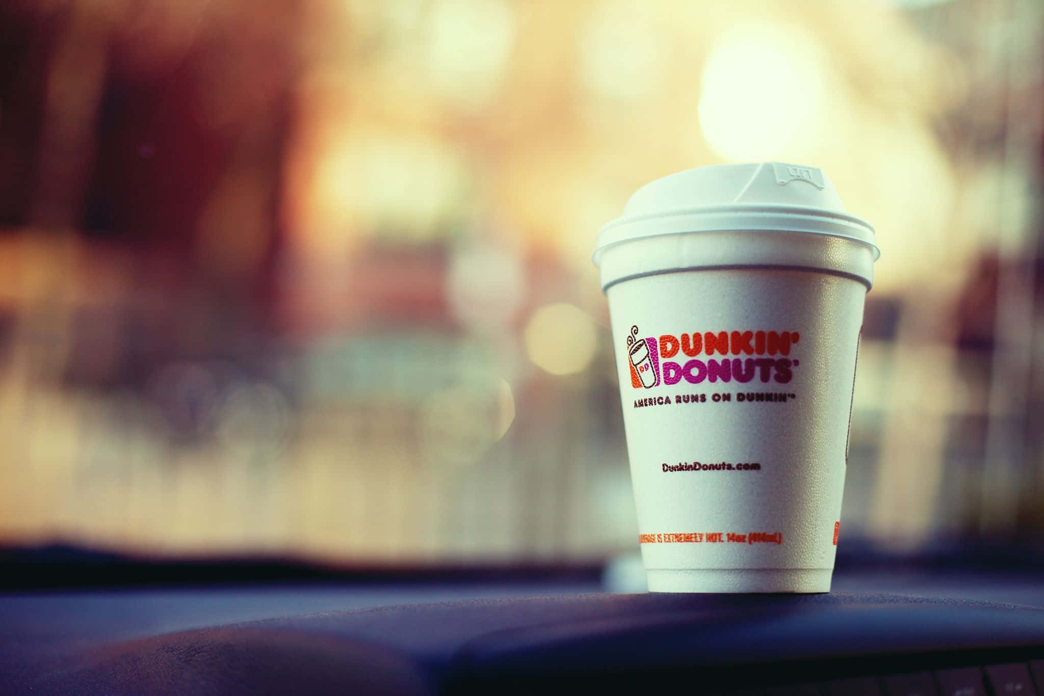 Dunkin Donuts 桌布 壁紙 — 一個Dunkin' Donuts咖啡杯放在黑暗的表面上，背景中溫暖的散景燈光柔和地發光。