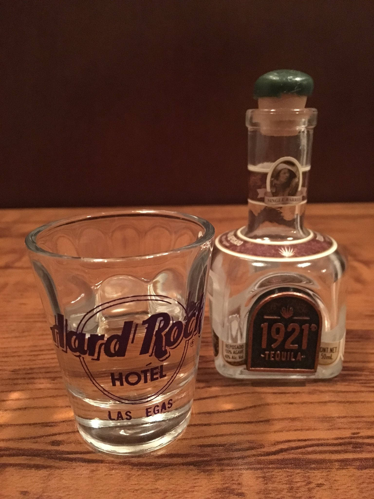 drinks 桌布 壁紙 — 一個Hard Rock Hotel Las Vegas的烈酒杯放在溫暖的木桌上，旁邊是一瓶迷你1921龍舌蘭酒。