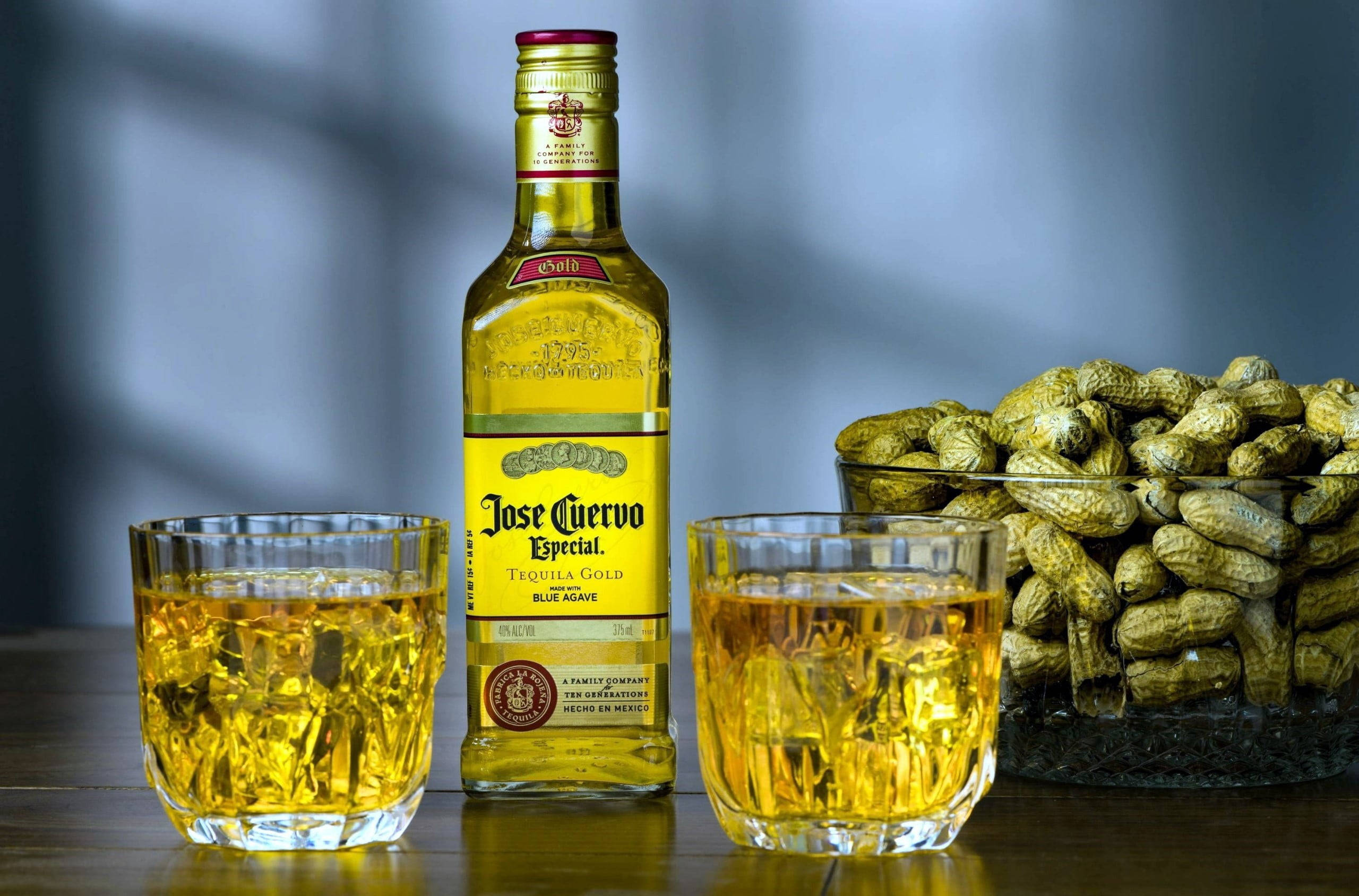 alcohol 桌布 壁紙 — 一個Jose Cuervo Tequila Gold酒瓶，兩個裝滿冰塊的玻璃杯，以及一碗花生放在木桌上。