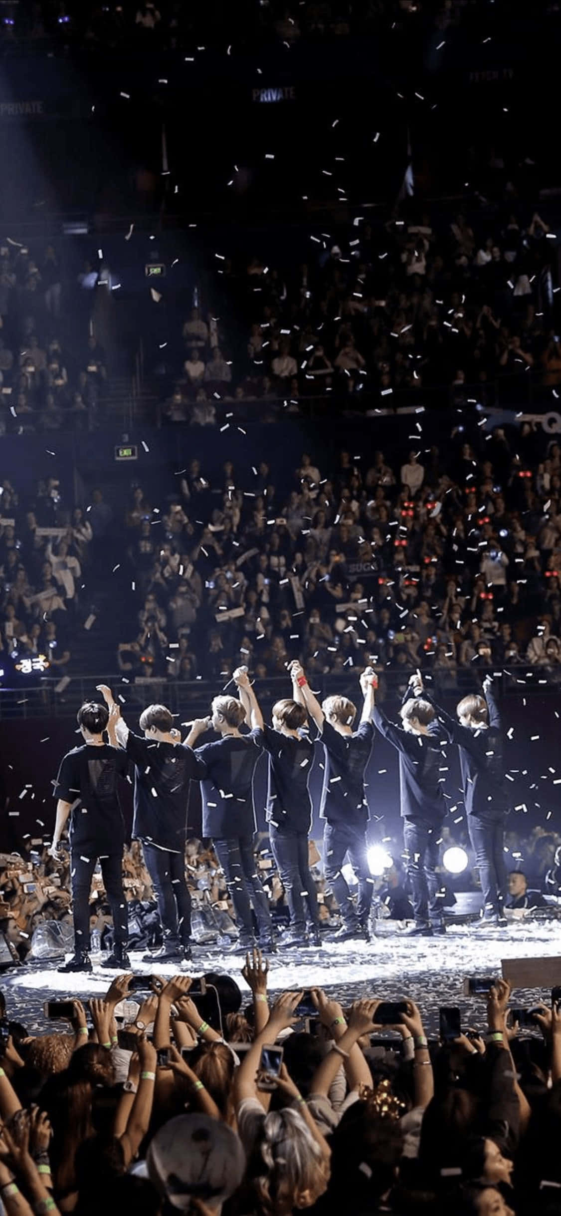 Bts Stage 桌布 壁紙 — 一個K-pop團體在明亮的燈光下於舞台上慶祝，五彩紙屑如雨般灑落在下方狂歡的人群中。
