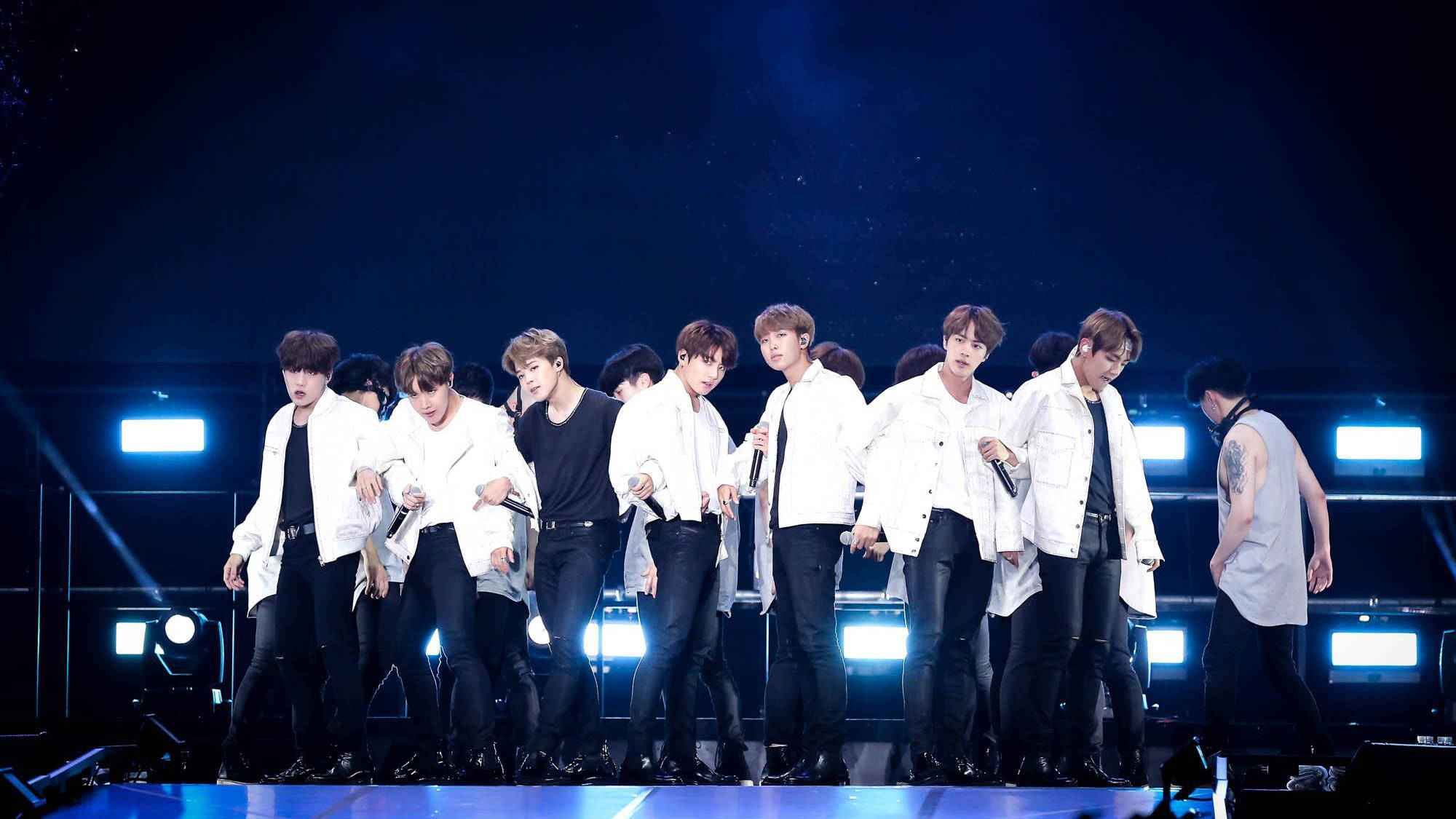 BTS 桌布 壁紙 — 一個K-pop組合在黑暗舞台上充滿活力地表演，舞台被明亮的藍色聚光燈和煙霧效果照亮。