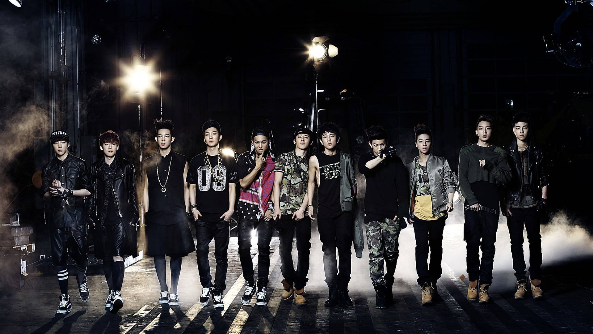 Ikon 桌布 壁紙 — 一個K-pop組合自信地站在煙霧瀰漫的黑暗錄影室中，被戲劇性的聚光燈照亮，投射出銳利的陰影。