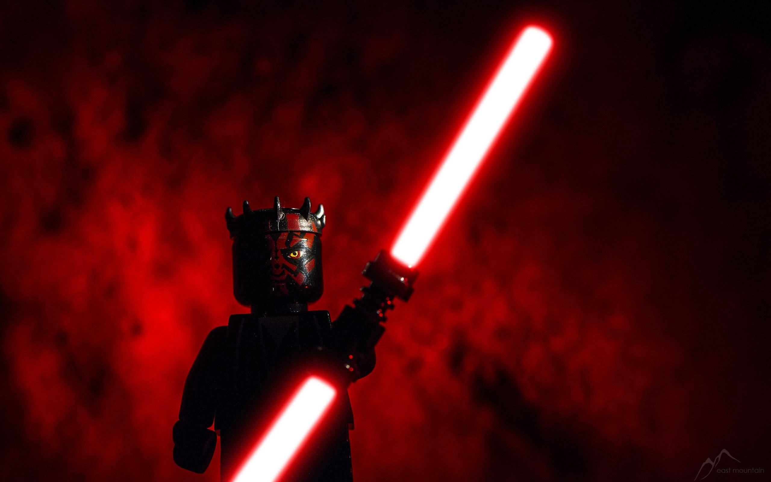 Maul 桌布 壁紙 — 一個LEGO Darth Maul人偶在煙霧瀰漫的深紅色背景下揮舞著發光的紅色光劍。