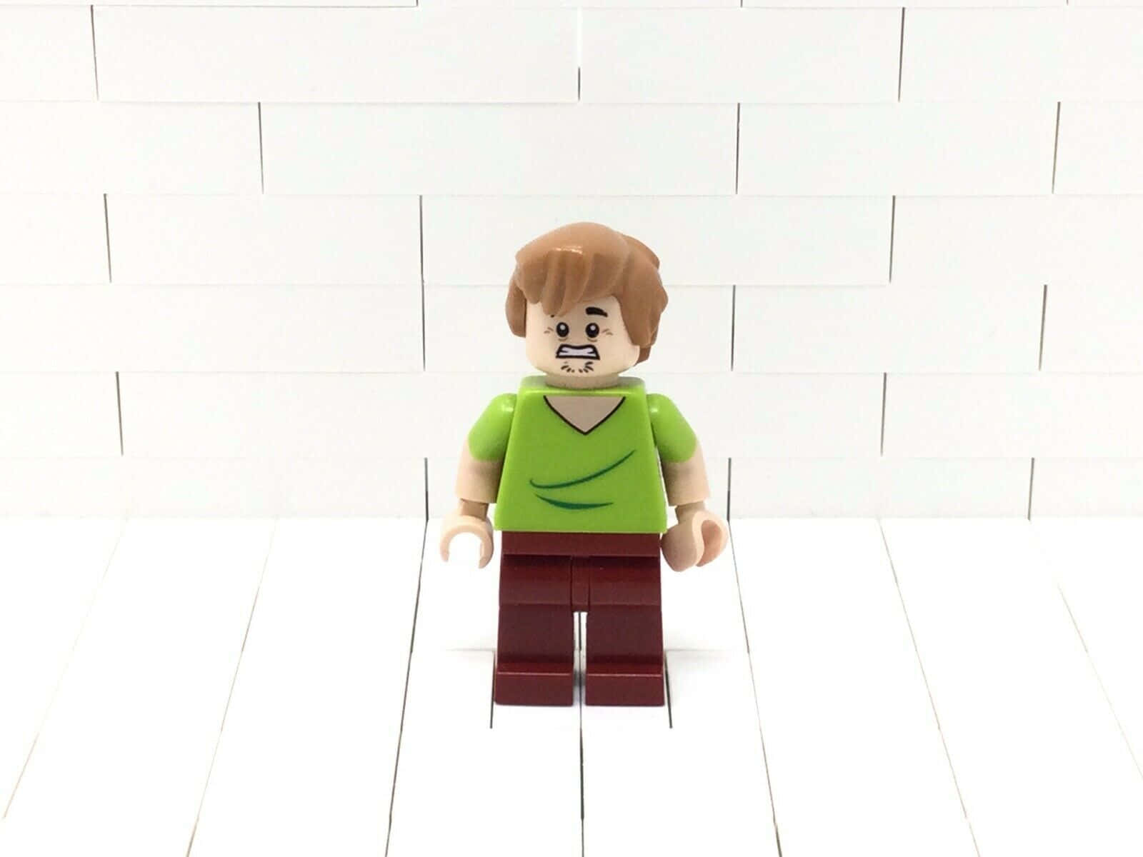 Shaggy Rogers 桌布 壁紙 — 一個LEGO弗雷德·弗林斯通人偶站在白色磚牆前，表情不悅。