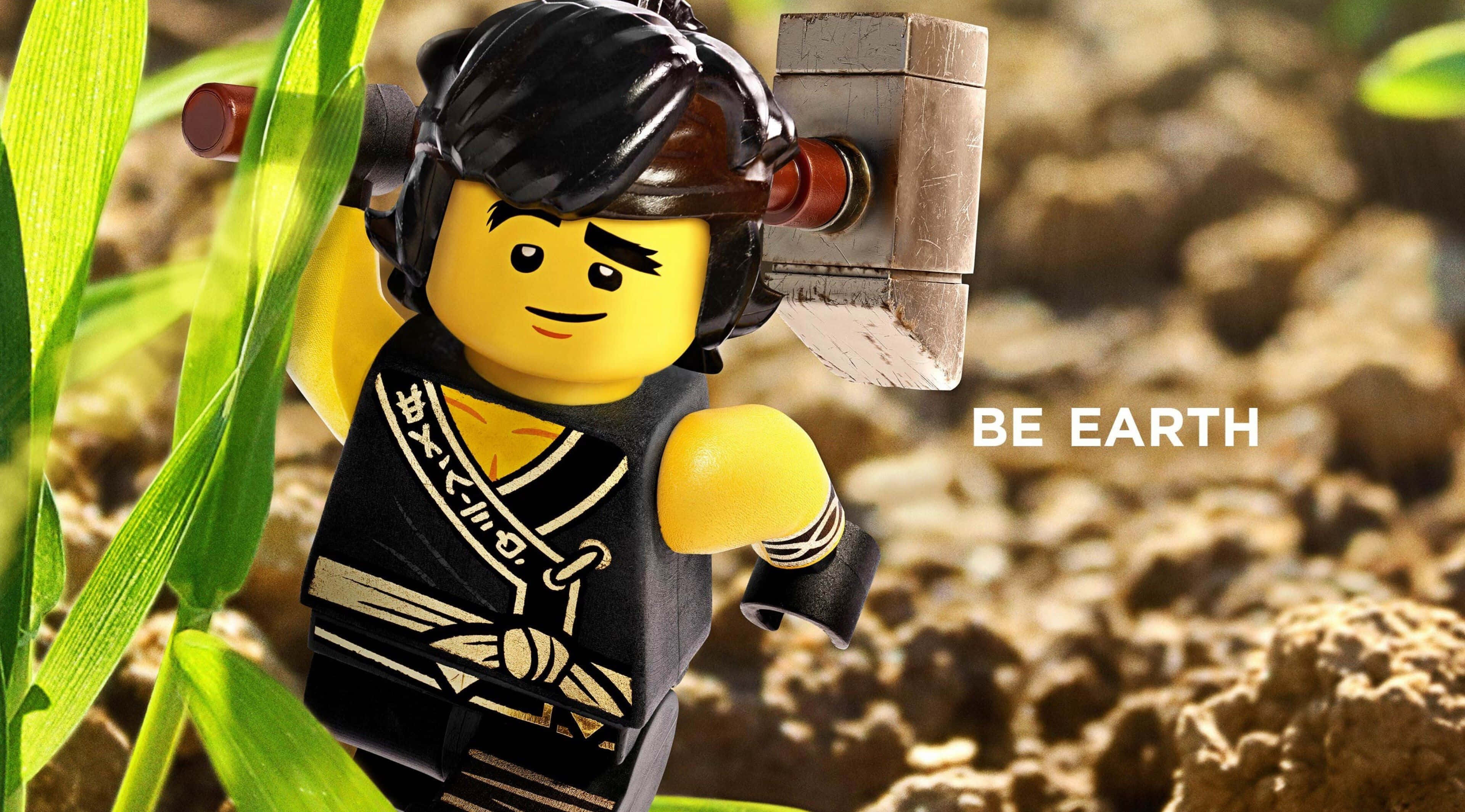 Ninjago 桌布 壁紙 — 一個LEGO旋風忍者大地忍者站在陽光照耀的草地上，手持石錘，附近有「BE EARTH」字樣。