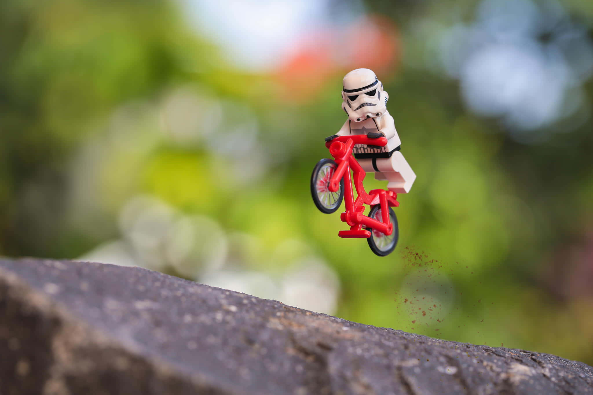 awesome cool 桌布 壁紙 — 一個LEGO白兵人偶在半空中騎著紅色腳踏車，從石頭邊緣跳下，背景是模糊的綠色樹葉。