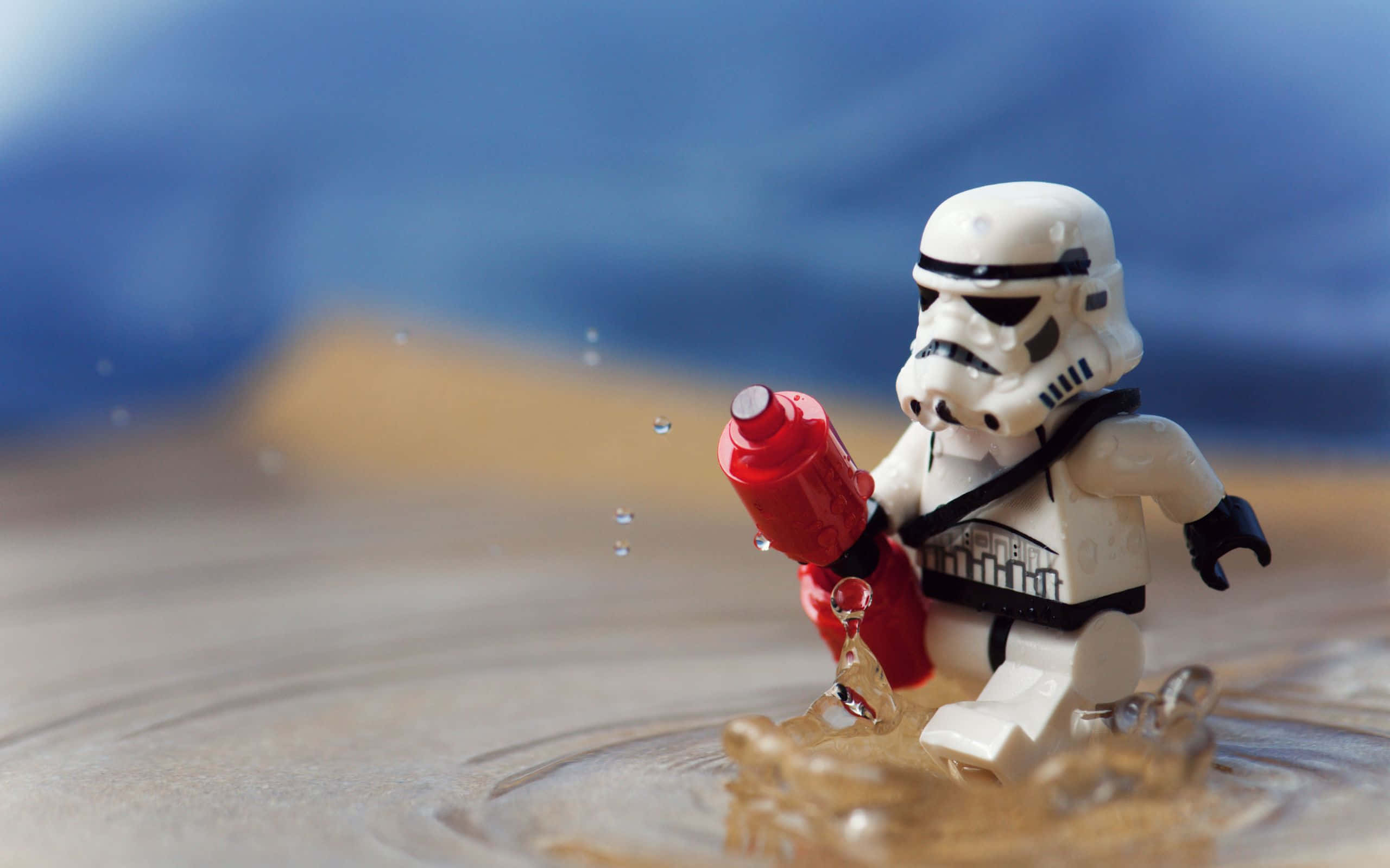 樂高 桌布 壁紙 — 一個LEGO風暴兵人偶站在淺水中，手持紅色玩具爆能槍，水滴在其腳邊飛濺。