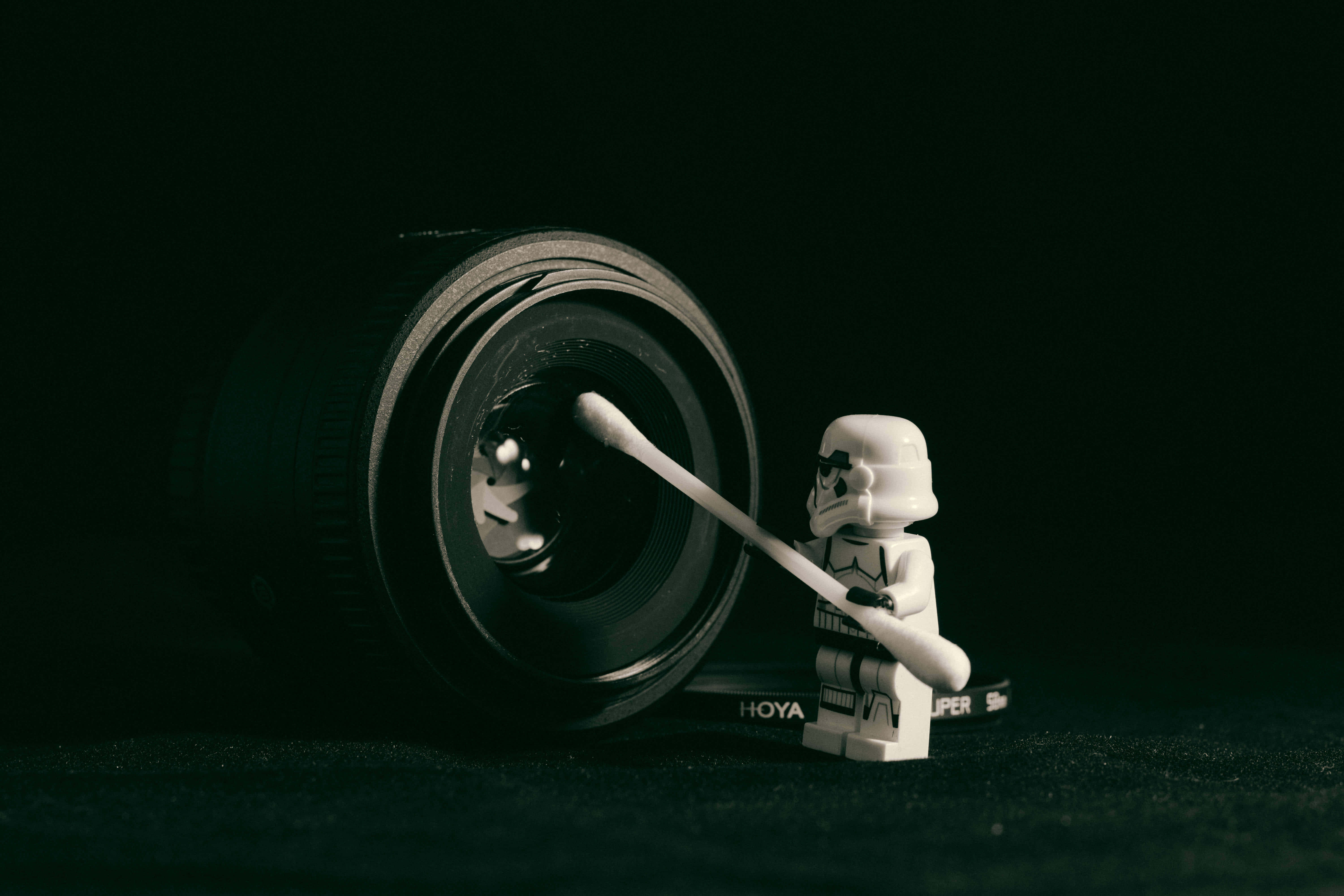 Funny Star Wars 桌布 壁紙 — 一個LEGO風暴兵正用棉花棒仔細清潔相機鏡頭，背景為純黑色。