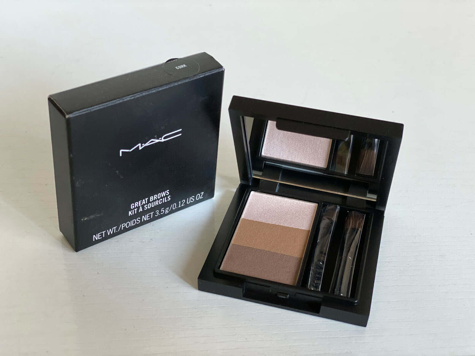 Mac Cosmetics 桌布 壁紙 — 一個MAC Great Brows套裝，內含三種棕色調和刷子，打開放在白色表面上，旁邊是其黑色盒子。
