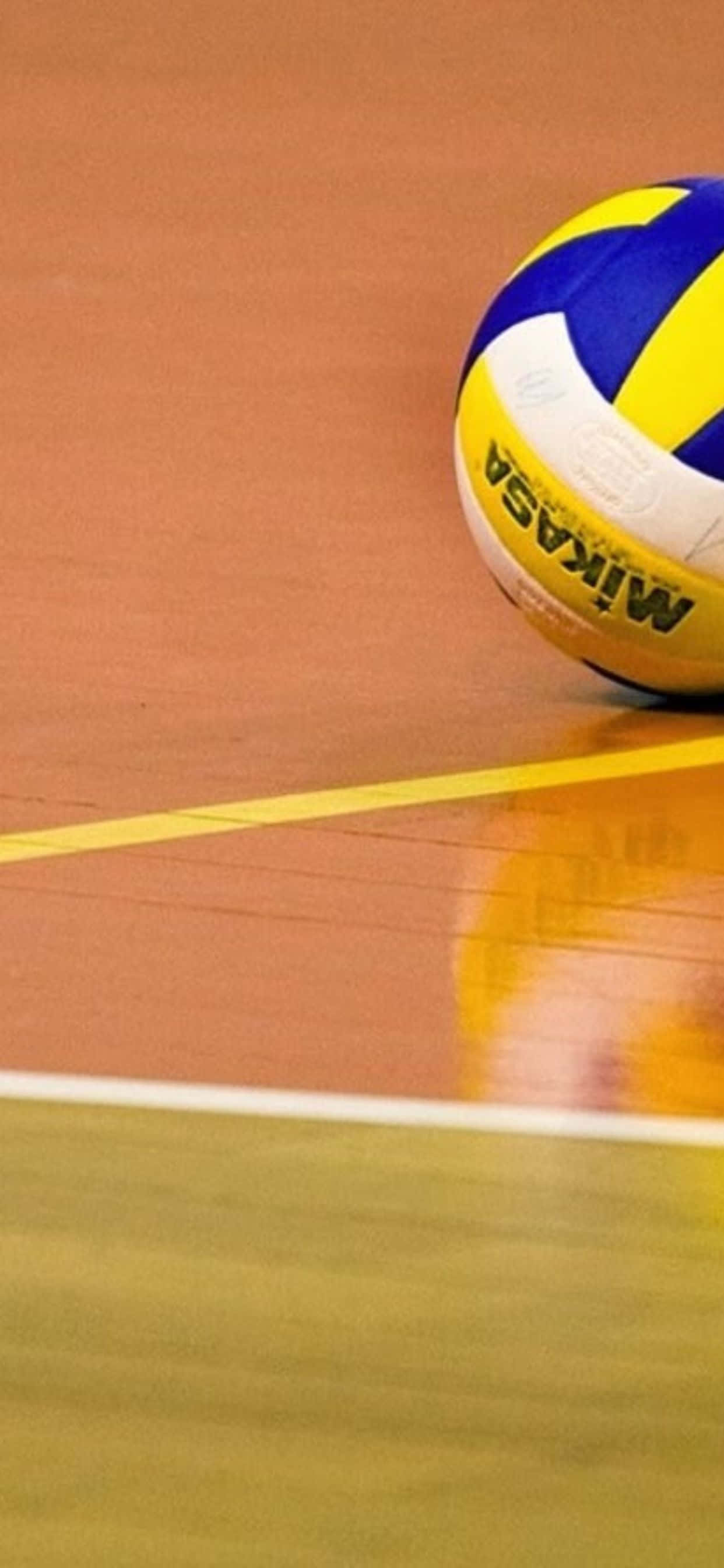 iPhone Xs Max Volleyball 桌布 壁紙 — 一個Mikasa排球放在一個拋光橙色、標有黃色和白色線條的球場上。