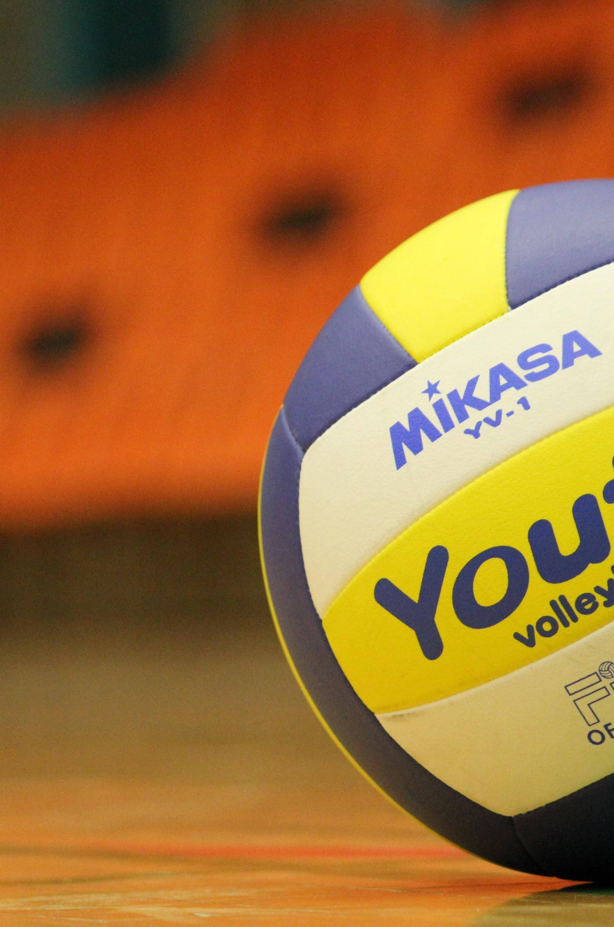 Volleyball Aesthetic 桌布 壁紙 — 一個Mikasa排球特寫，放在木地板上，背景有模糊的橙色看台。