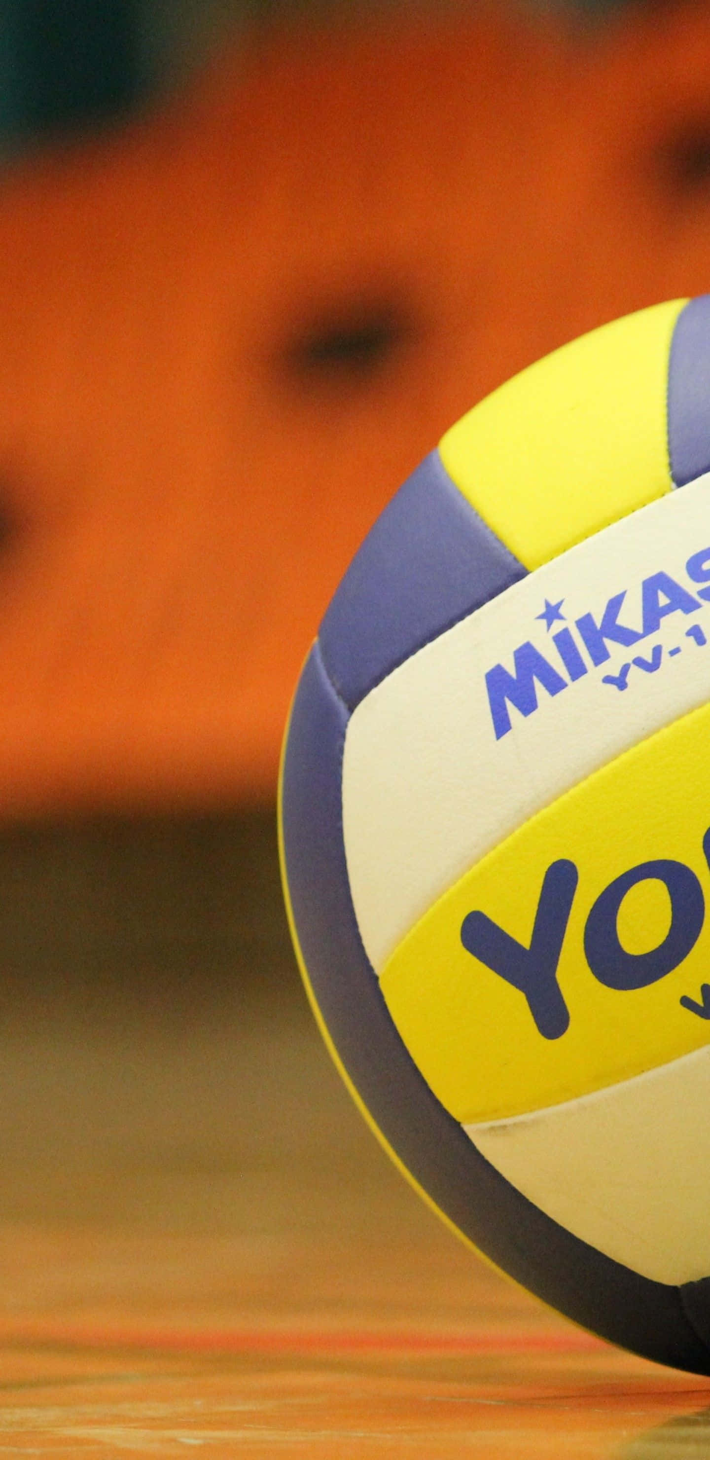 Volleyball 桌布 壁紙 — 一個Mikasa排球的特寫，放在木質球場上，背景是溫暖的橙色模糊效果。