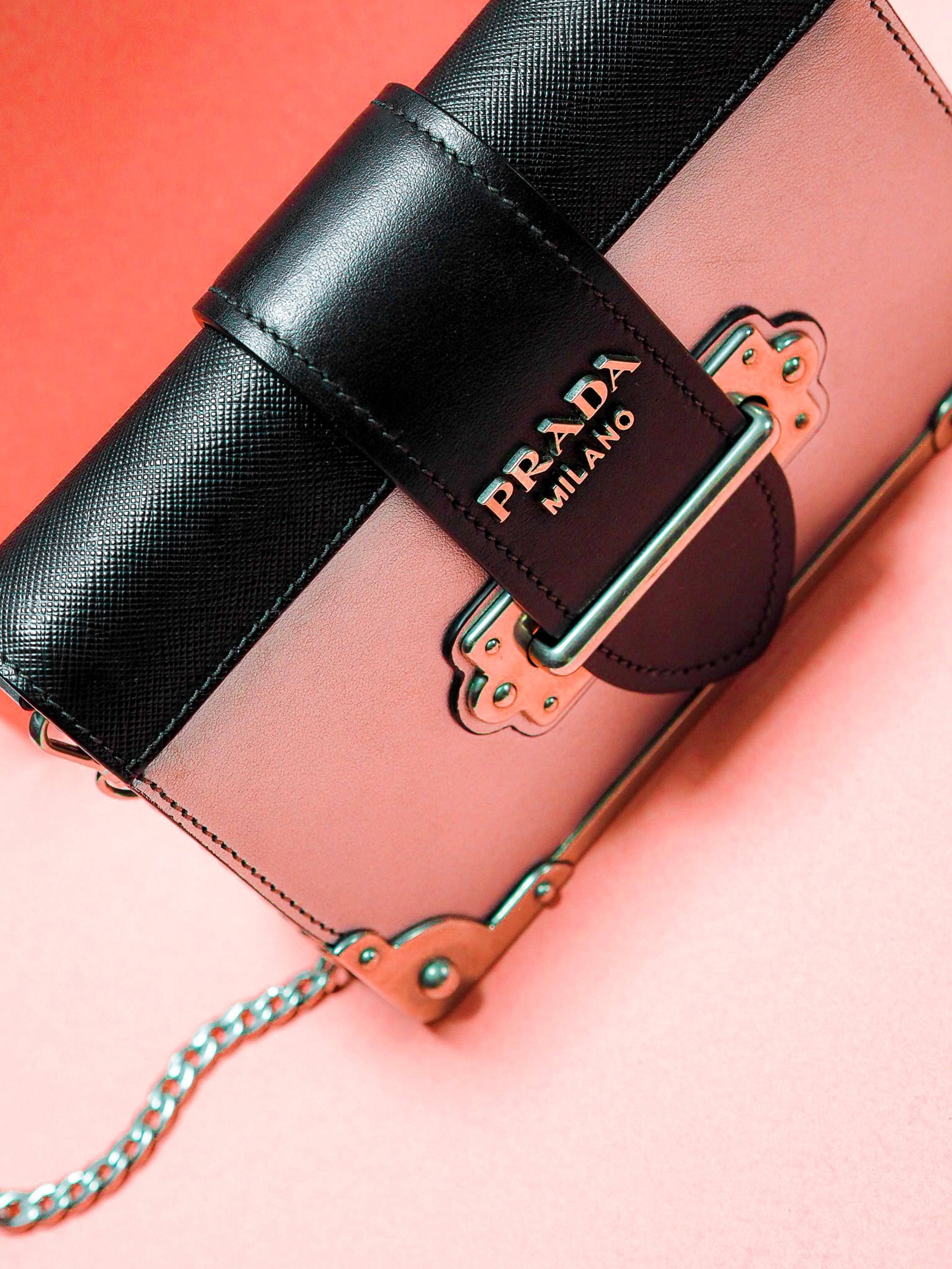 Prada 桌布 壁紙 — 一個Prada手提包，配有黑色和粉紅色皮革肩帶及金屬配件，放在珊瑚粉紅色背景上。