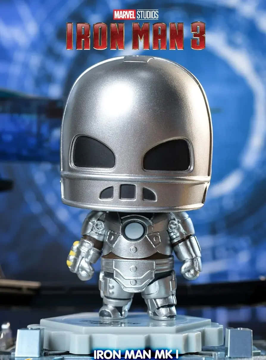 Iron Man Bobbleheads 桌布 壁紙 — 一個Q版風格的鋼鐵人MK I動作人偶站在灰色底座上，背景是帶有電影標題文字的藍色模糊背景。
