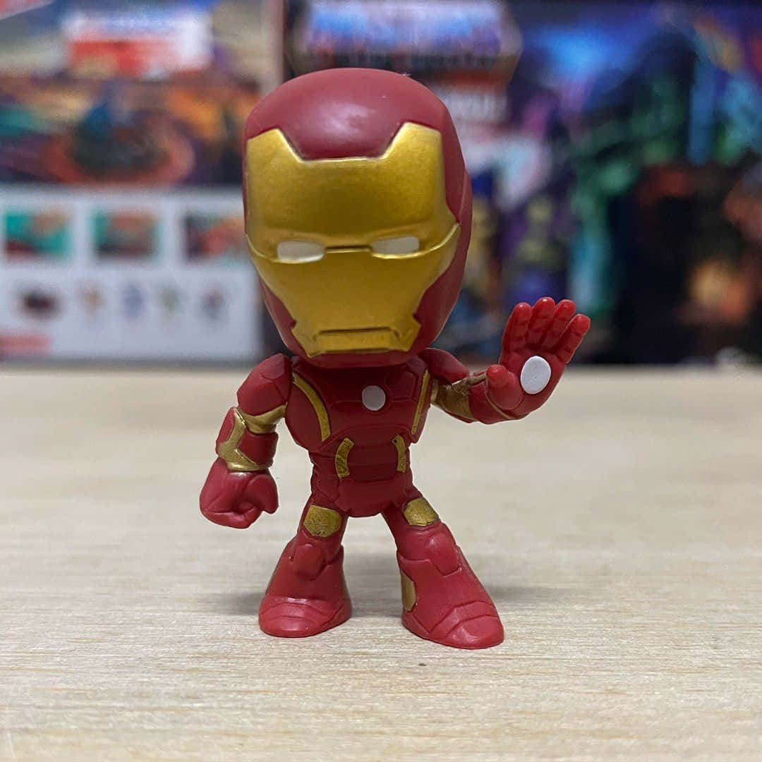Iron Man Bobbleheads 桌布 壁紙 — 一個Q版風格的鋼鐵人動作人偶站在木質表面上，背景是模糊的漫畫書。