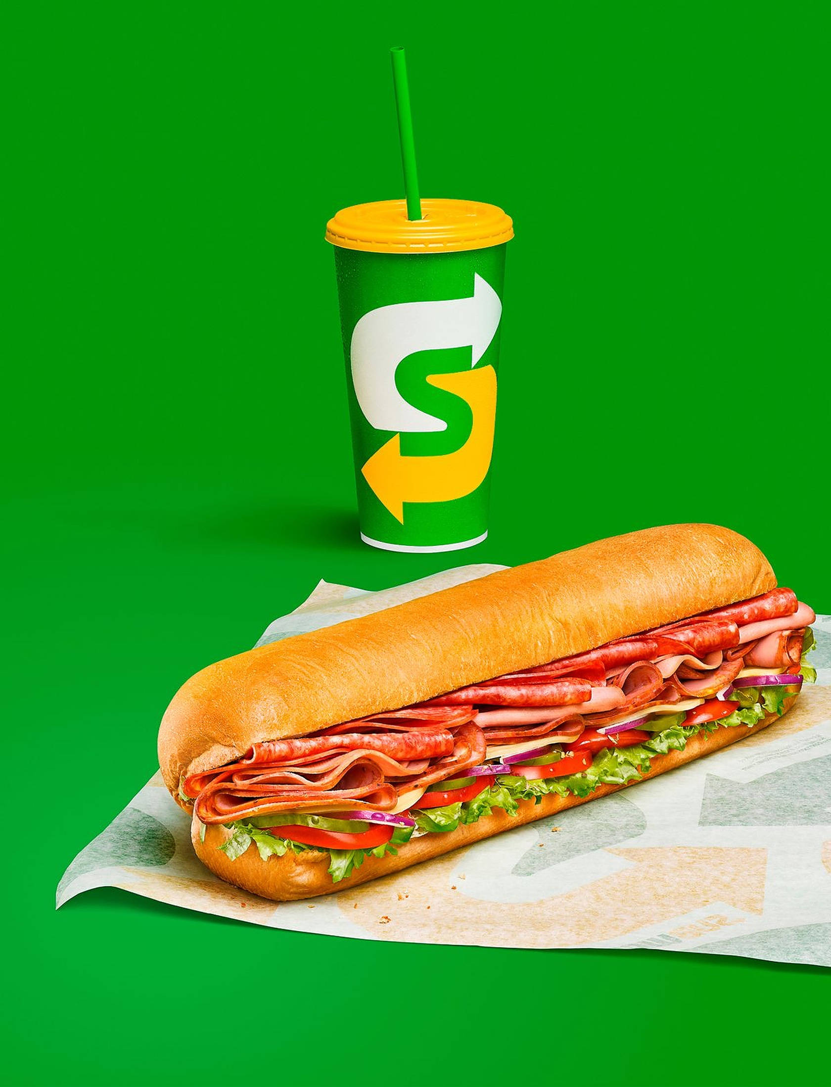 三明治 桌布 壁紙 — 一個Subway三明治和飲料杯放在充滿活力的綠色背景上，展示新鮮食材和大膽的品牌形象。